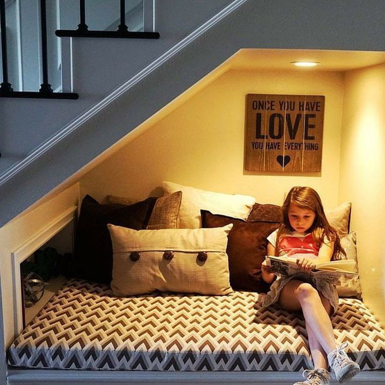 A child reading on a built-in bench with a chevron cushion and pillows under the stairs.