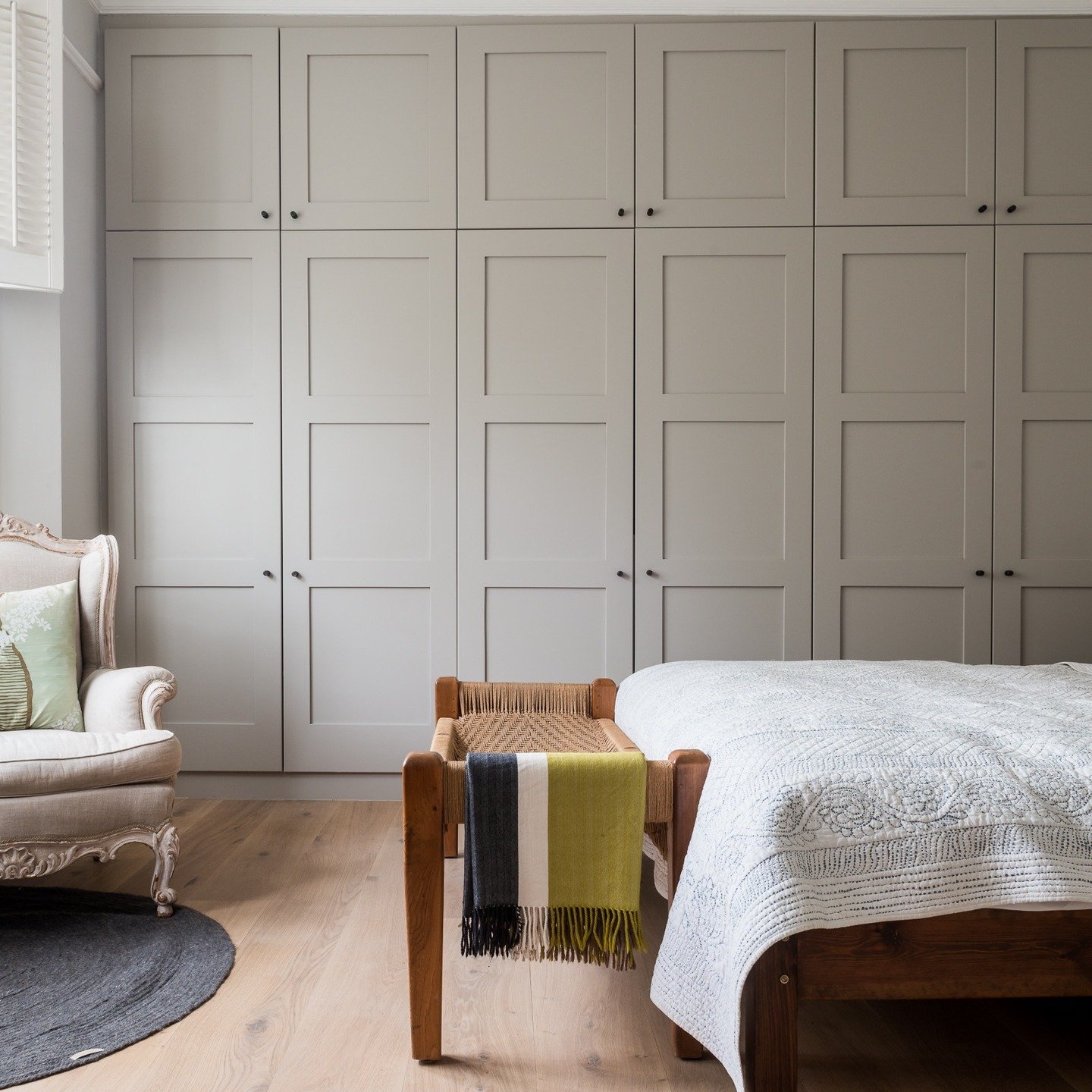 Large floor-to-ceiling built-in wardrobe with shaker-style paneling in a neutral greige color, featuring small black knobs and upper cabinets.