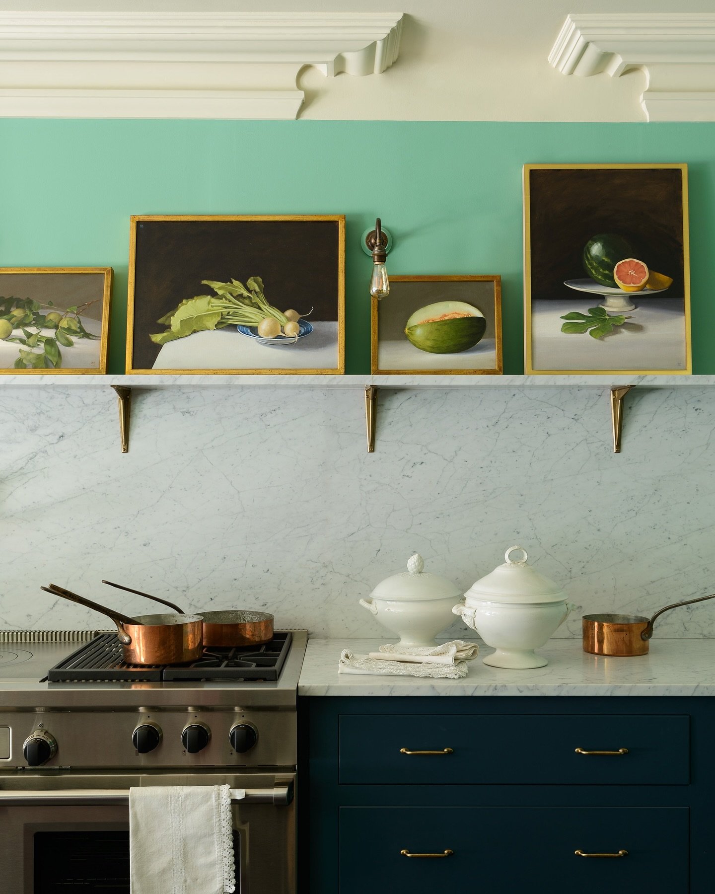 A framed portrait or figurative painting hanging on a dark gray wall in a classic kitchen with a large wooden table.