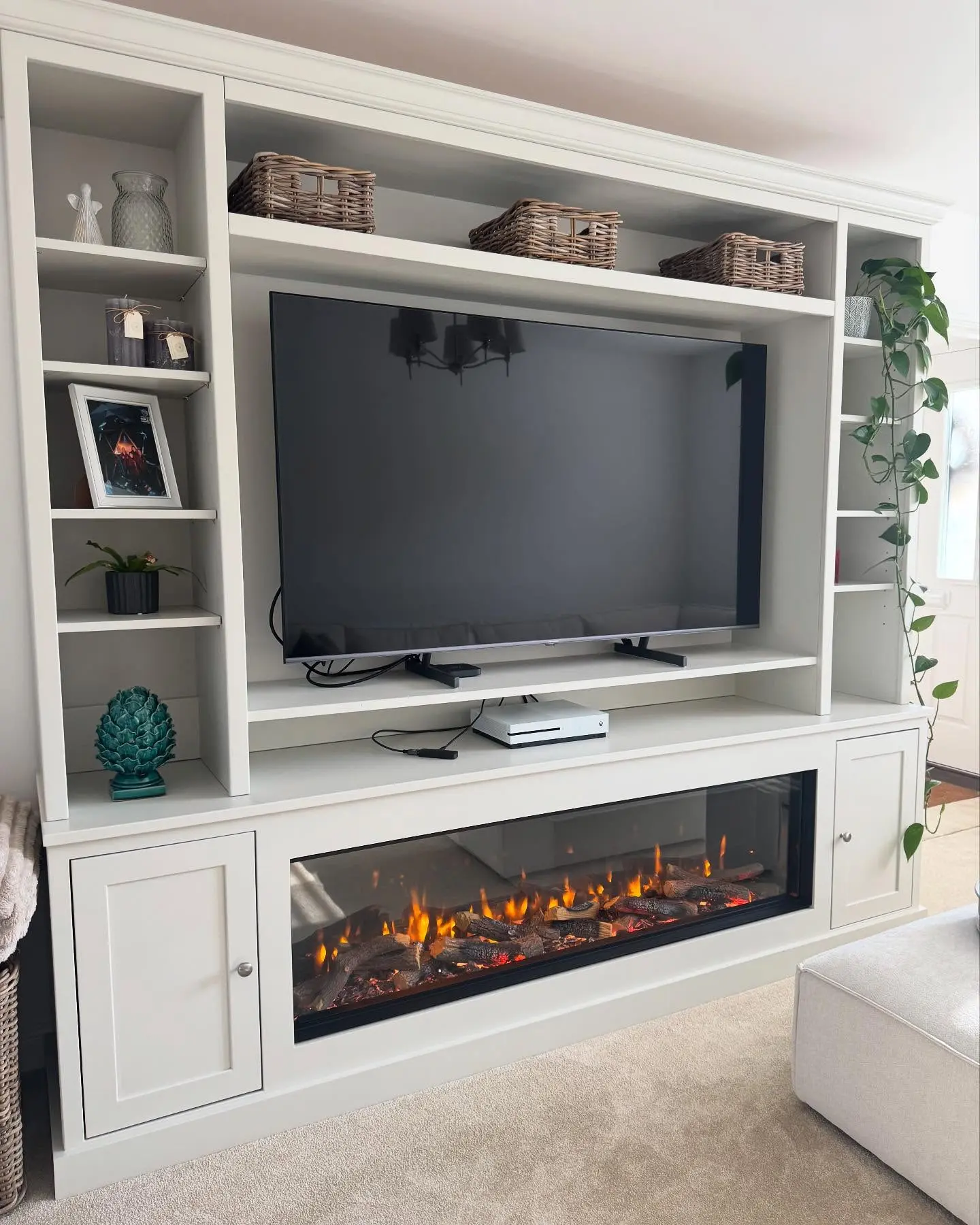 Large custom built-in white entertainment center with flanking open bookshelves and bottom cabinets, housing a wide linear electric fireplace and a flatscreen TV.