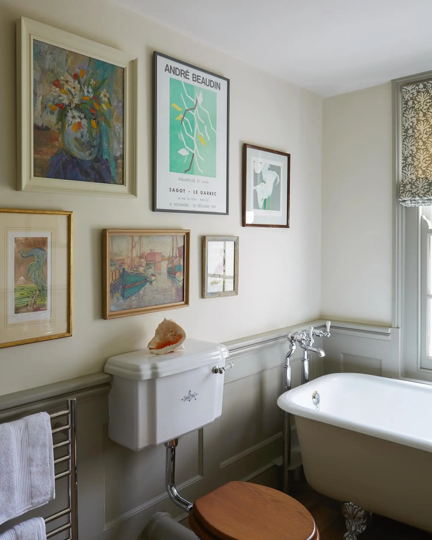 A traditional bathroom with light gray wainscoting, featuring a dynamic gallery wall of mixed sizes, frame styles, and subjects, including a still life, a poster, and a seascape.
