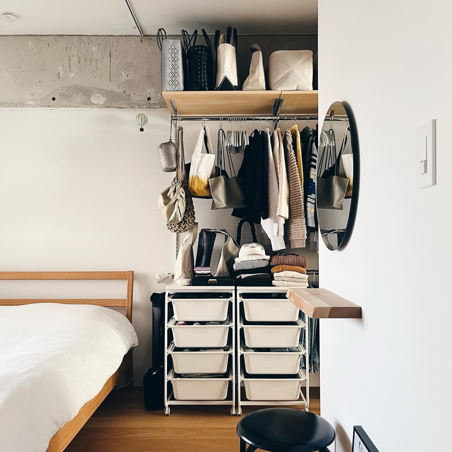 Small bedroom featuring an open closet system with a hanging rod, a high wooden shelf for bags, and two rolling drawer units with shallow white plastic bins.