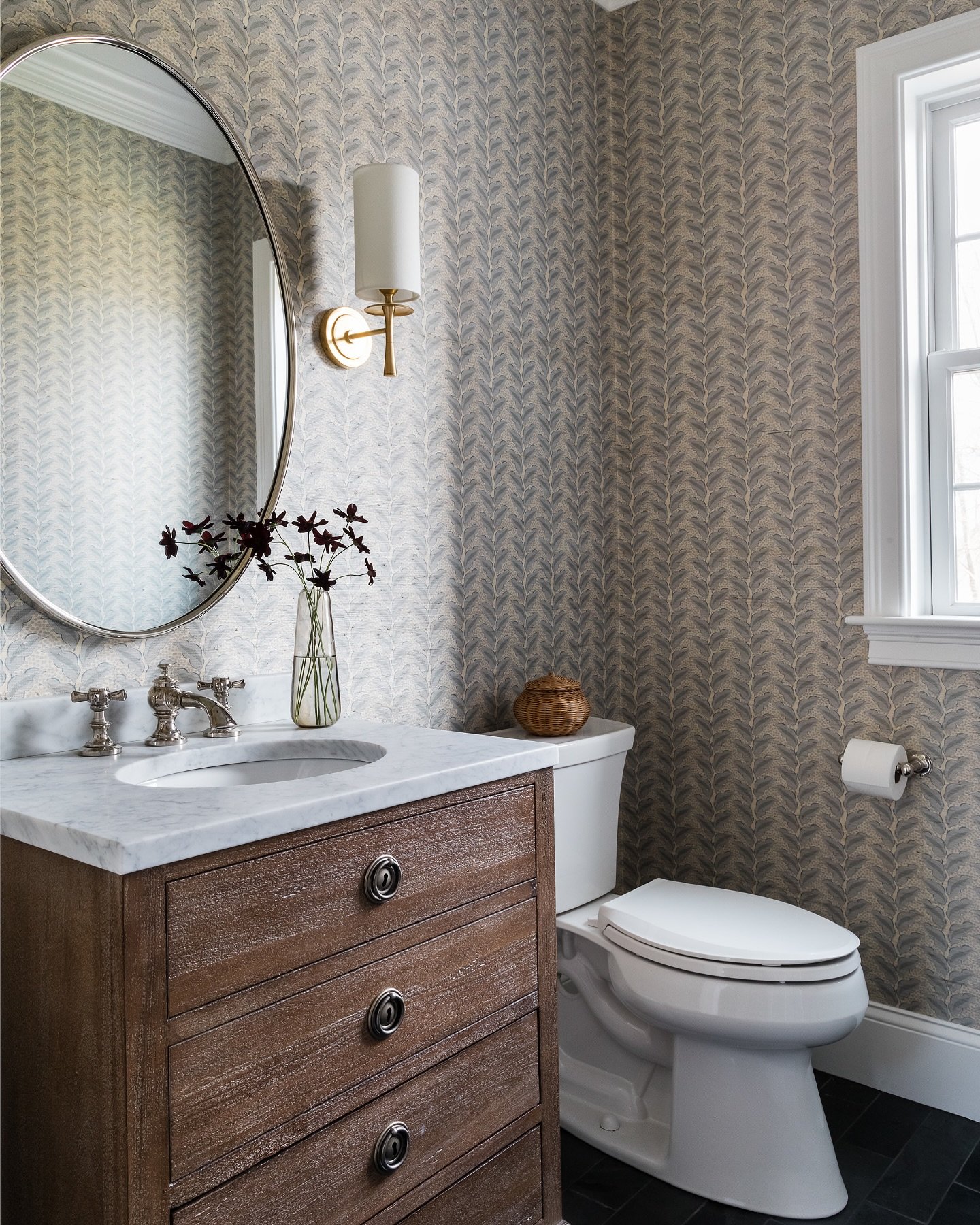 Powder room with a dark wood vanity, white marble top, and walls covered in a subtle blue and white fern or feather patterned wallpaper.