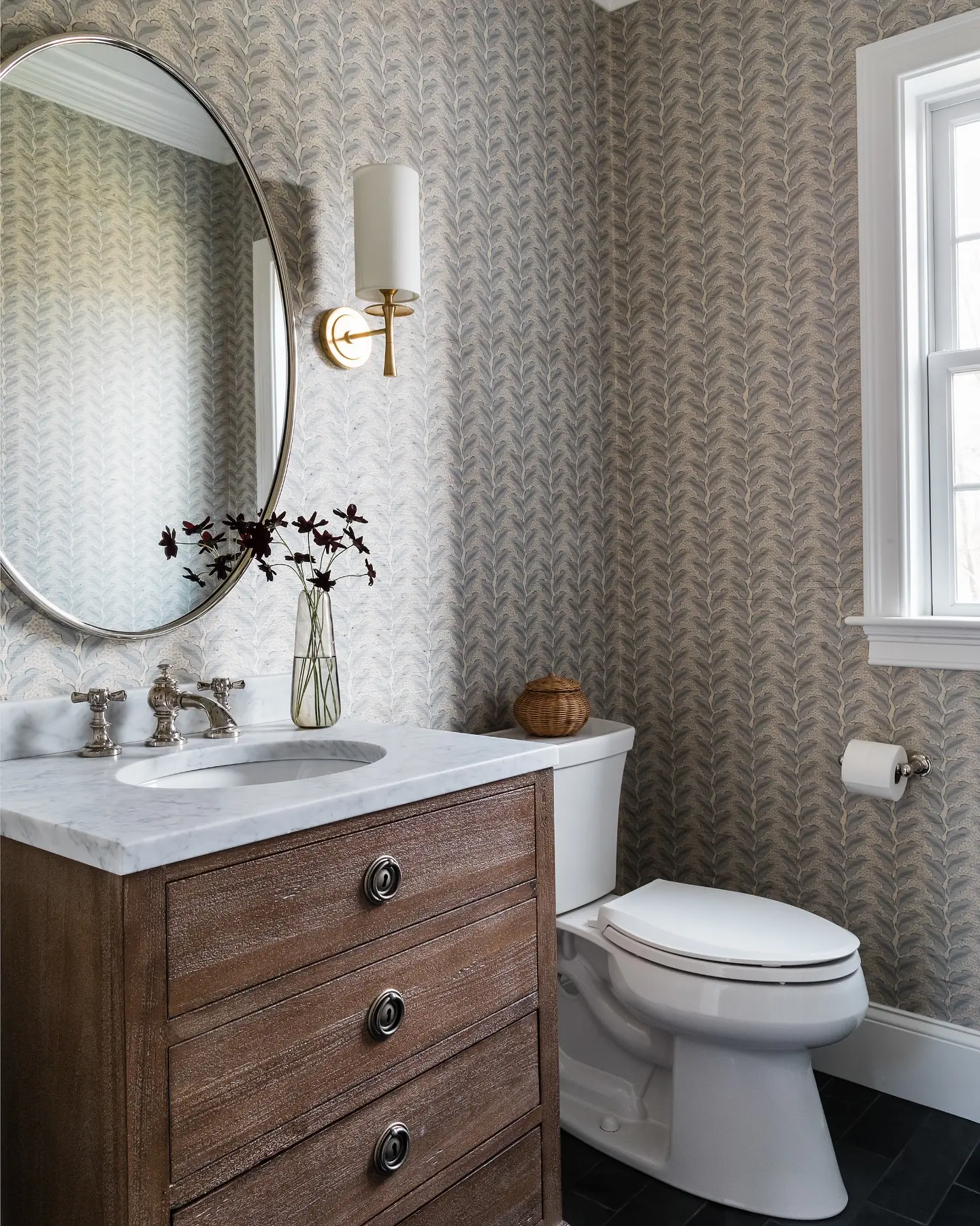 Powder room with a dark wood vanity, white marble top, and walls covered in a subtle blue and white fern or feather patterned wallpaper.
