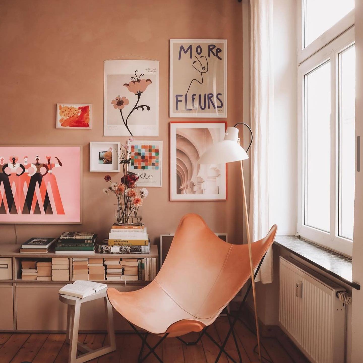 Eclectic and artistic reading nook with a cognac leather butterfly chair, a gallery wall of abstract and floral art, and a small console table with books