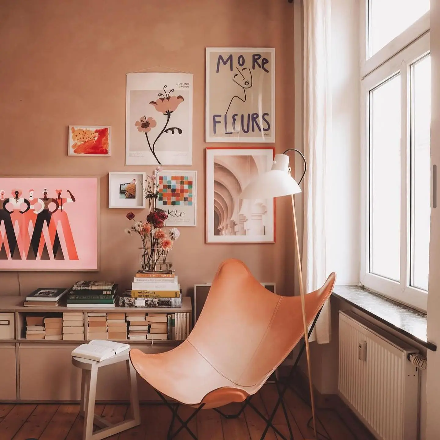Eclectic and artistic reading nook with a cognac leather butterfly chair, a gallery wall of abstract and floral art, and a small console table with books