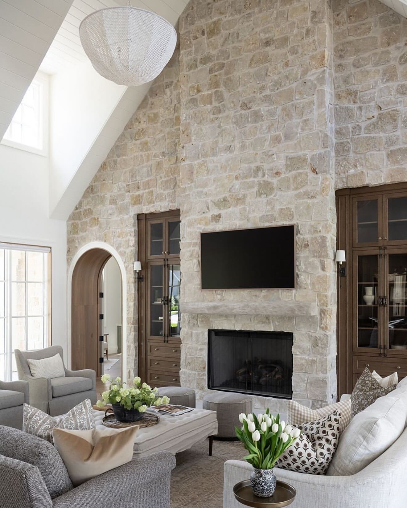 Grand living room with a full-height vaulted ceiling and fireplace clad in natural textured stone, flanked by dark wood built-in cabinets.