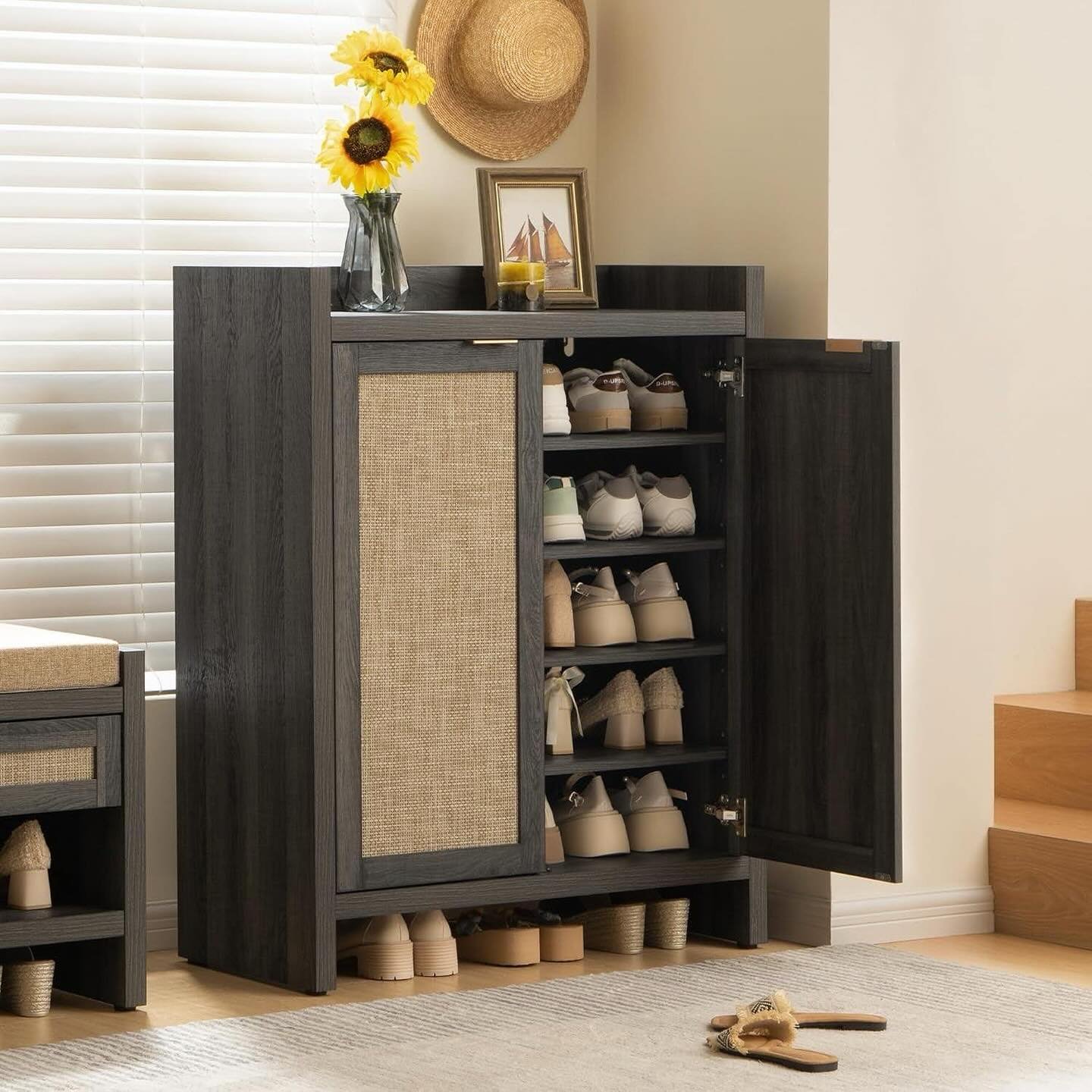 Rustic, dark grey wooden shoe cabinet with a rattan-style door panel, shelves visible inside storing multiple shoes.