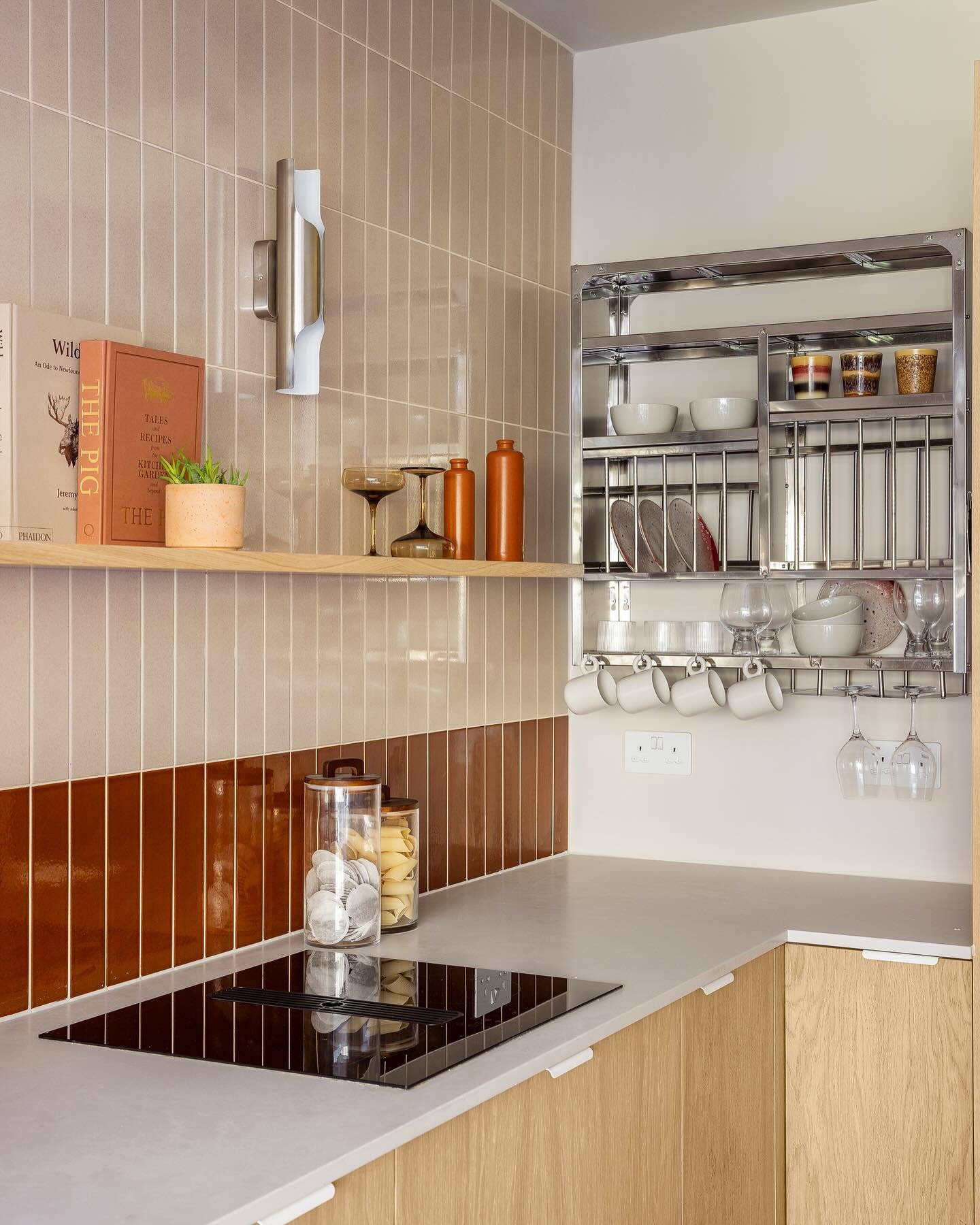 Modern kitchen with two-toned tiled wall featuring a stainless steel wall-mounted dish rack holding plates, bowls, cups, and wine glasses above the counter.