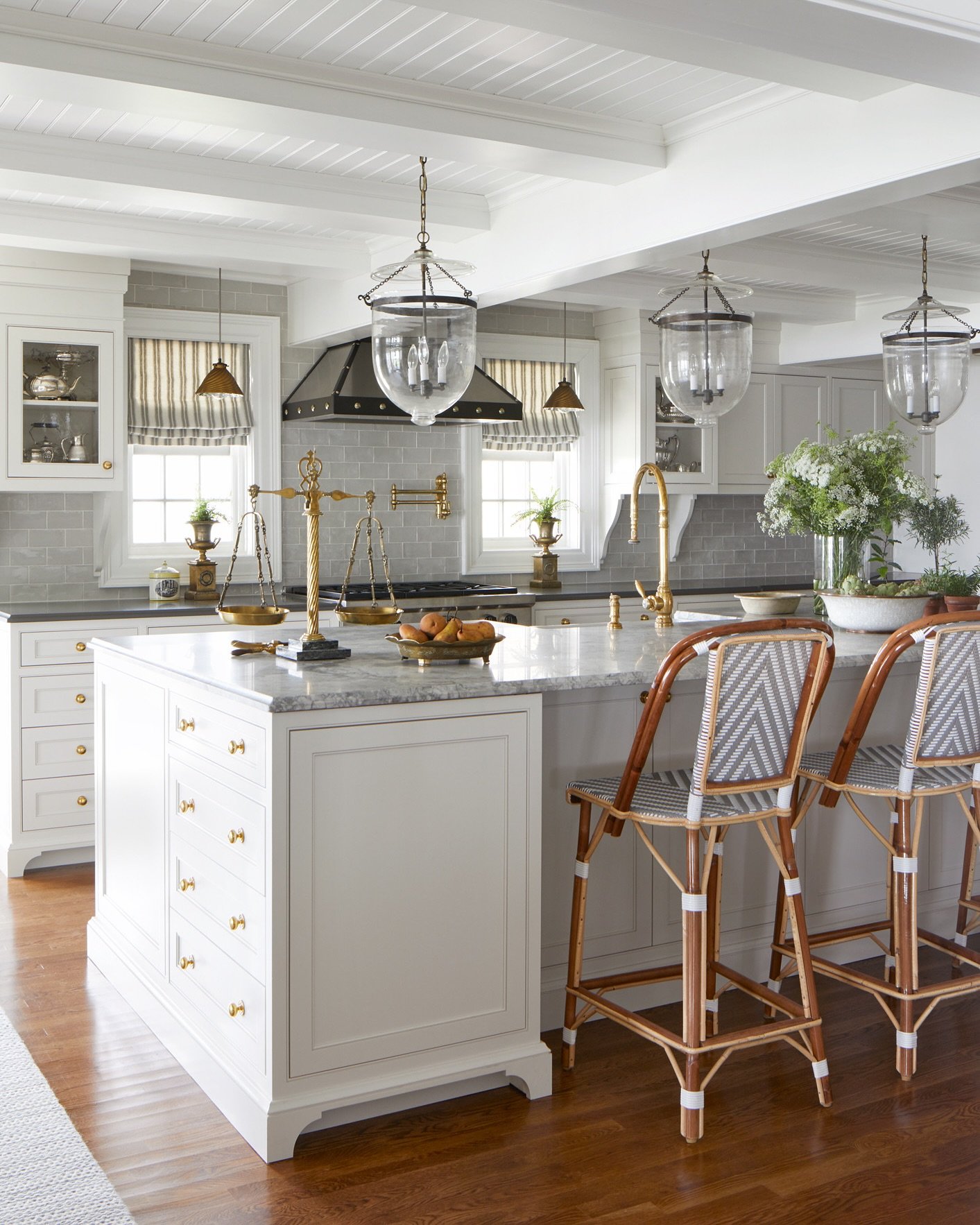 Traditional style kitchen featuring white inset cabinets, a beaded ceiling, brass hardware and faucet, antique lantern pendants, and rattan counter stools.