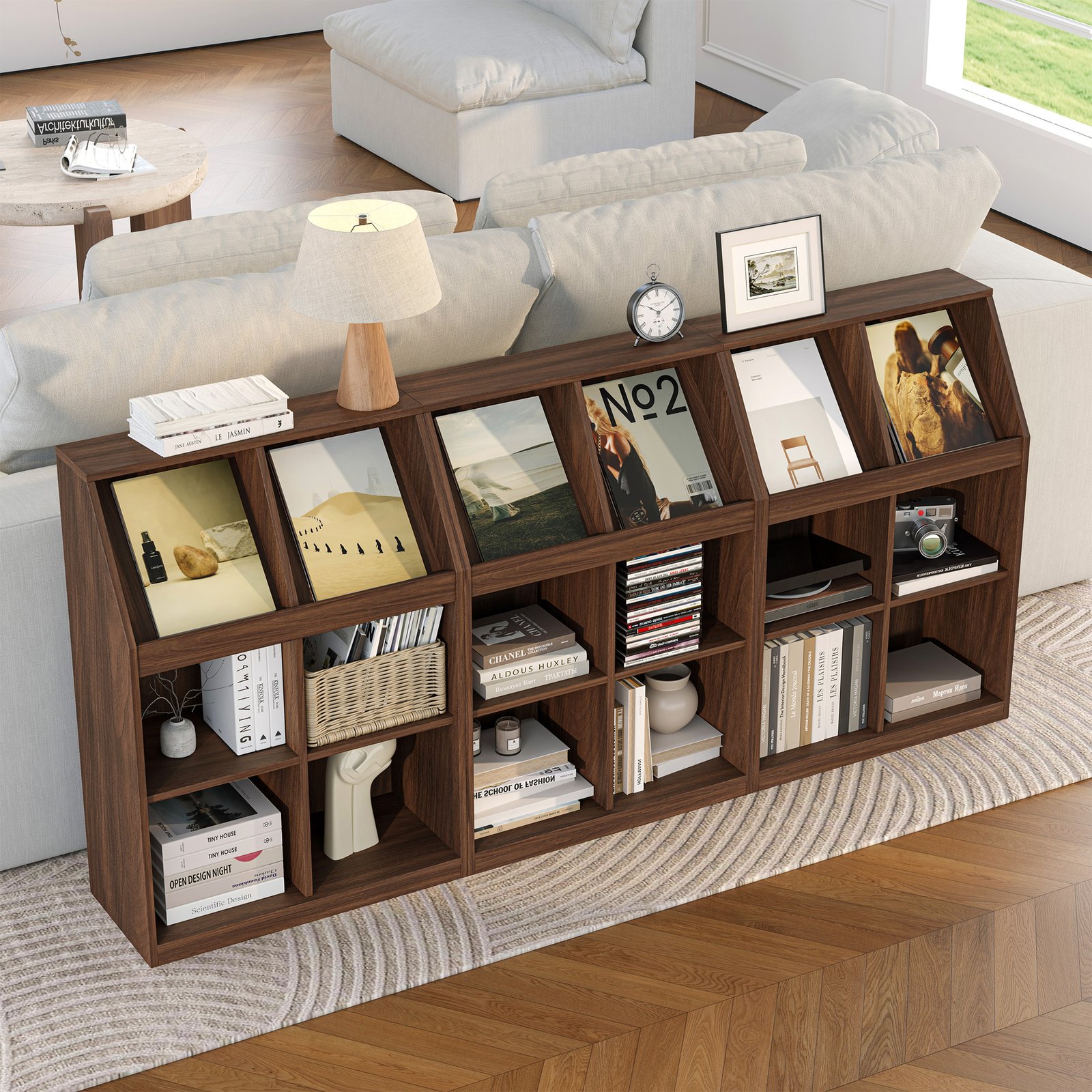 A long, low, dark wood console unit placed behind a white sofa, featuring angled slots on top for displaying magazines or large format books, and open shelving below for smaller books and storage baskets.
