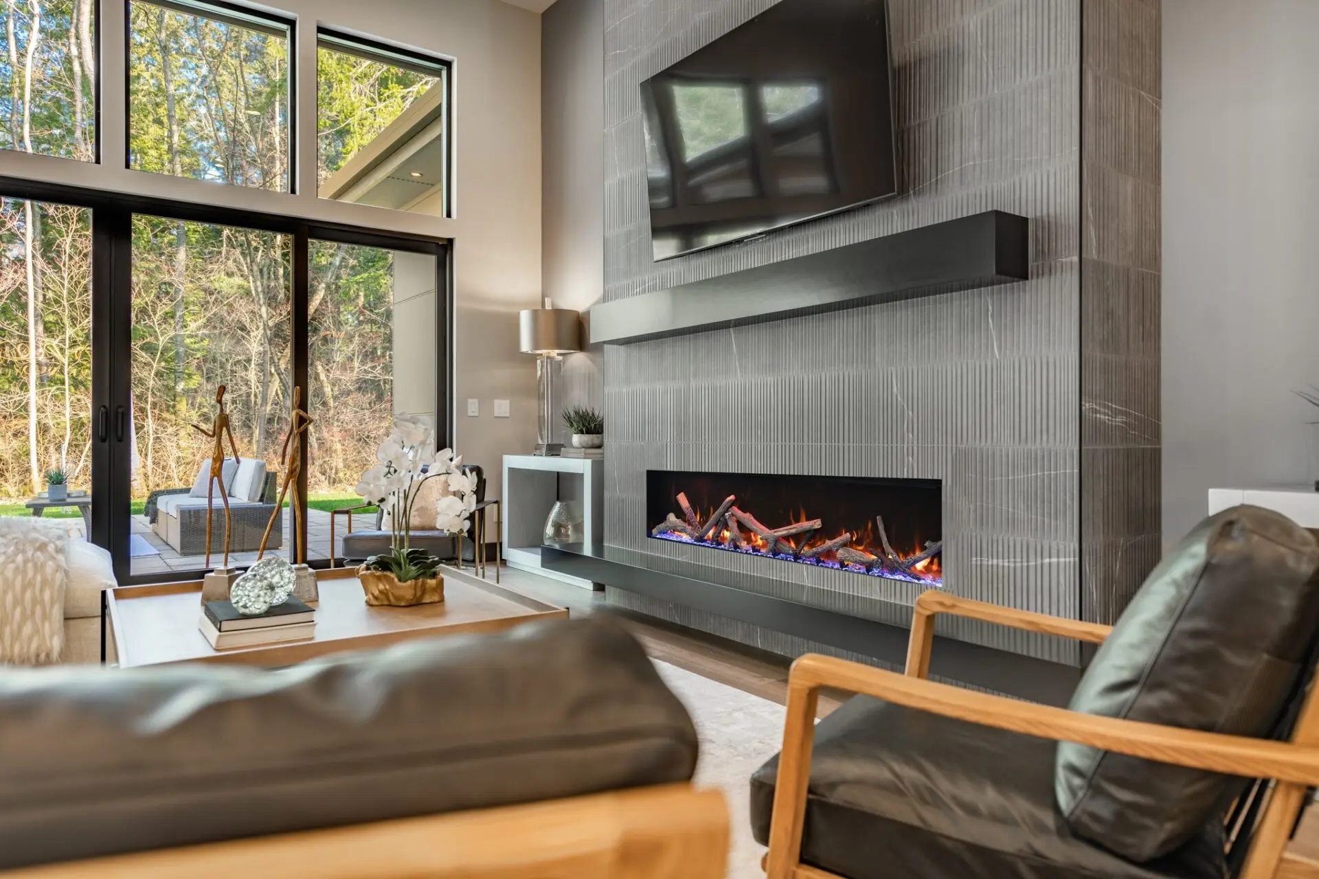 Contemporary living room with a feature wall covered in grey textured vertical tiles, a wide linear electric fireplace with blue flames, a large black floating mantel, and a mounted TV.
