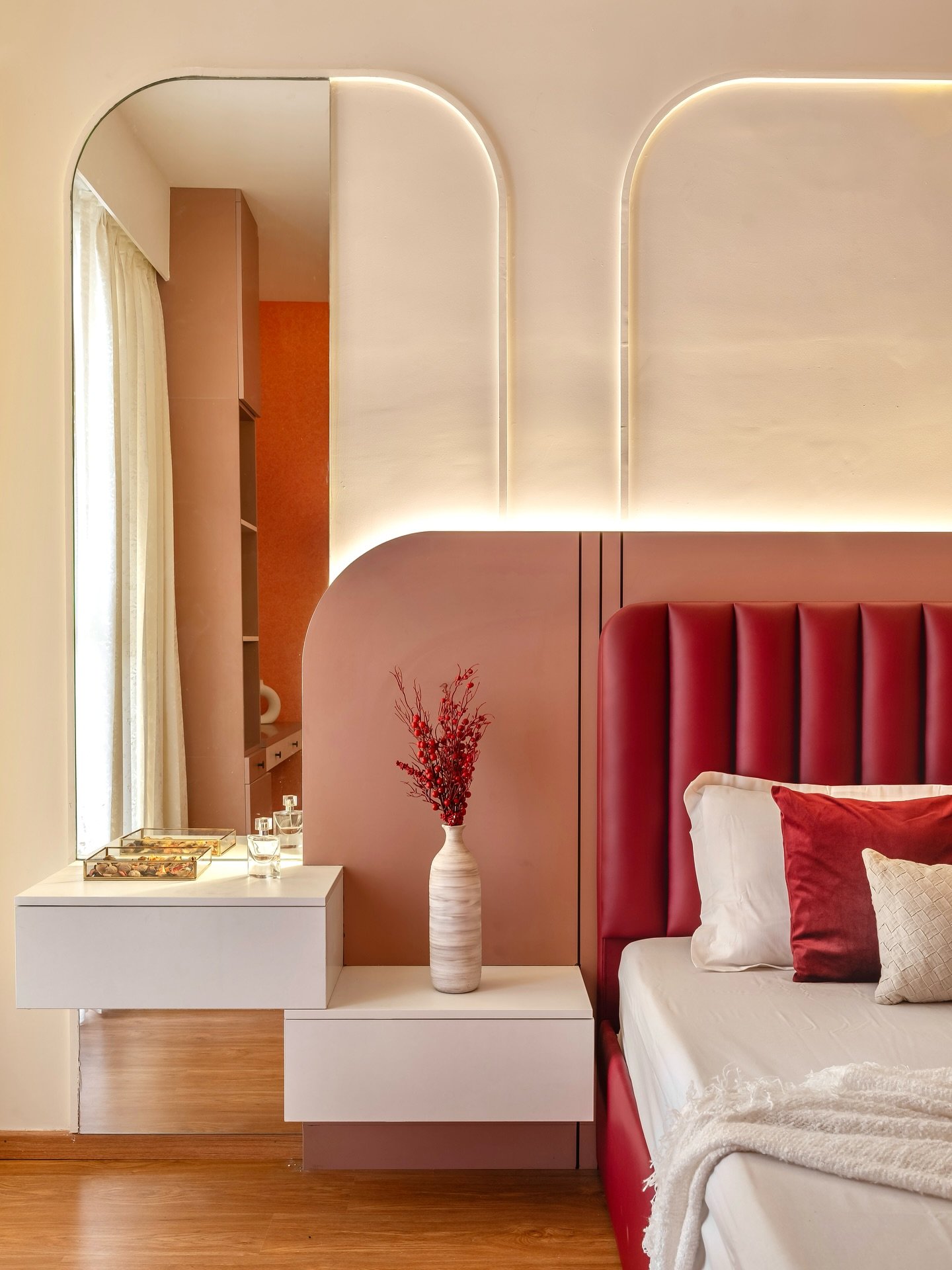 Custom wall paneling featuring a deep red leather channel tufted headboard, set beneath a curved, built-in panel of dusty rose and white with subtle integrated lighting and mirrored arches.