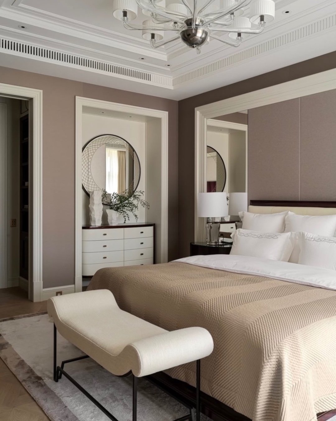 An elegant, transitional bedroom with a neutral color scheme and a sculptural modern bench with a white cushion and dark metal base at the foot of the bed.