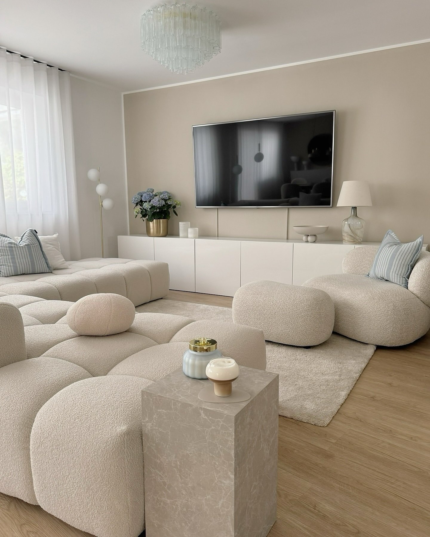 A contemporary neutral living room featuring a curved, low modular sofa and armchairs upholstered in white bouclé fabric, set against a tan accent wall.