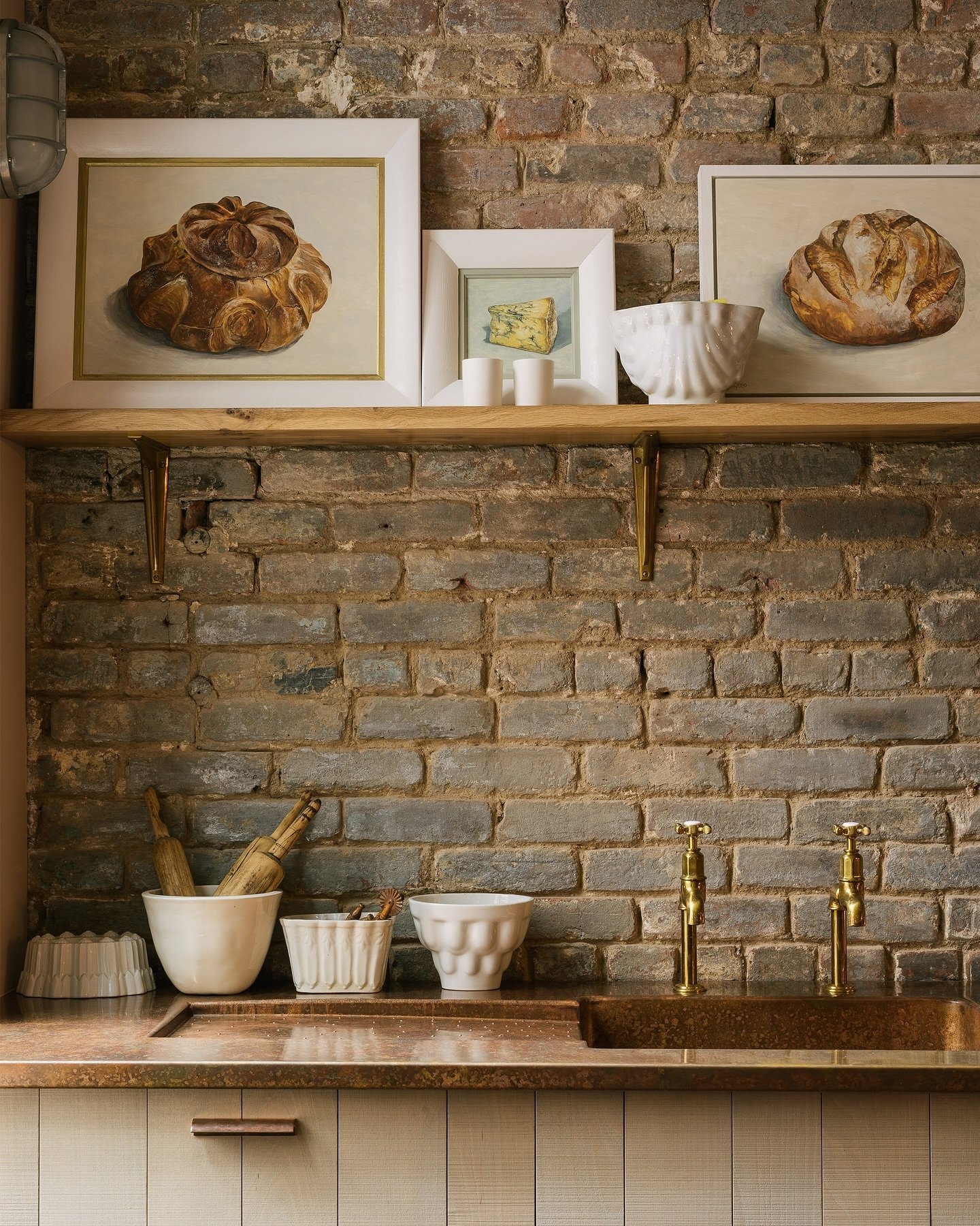 A small framed painting hanging directly above the kitchen window and sink area in a traditional, dark-toned kitchen.