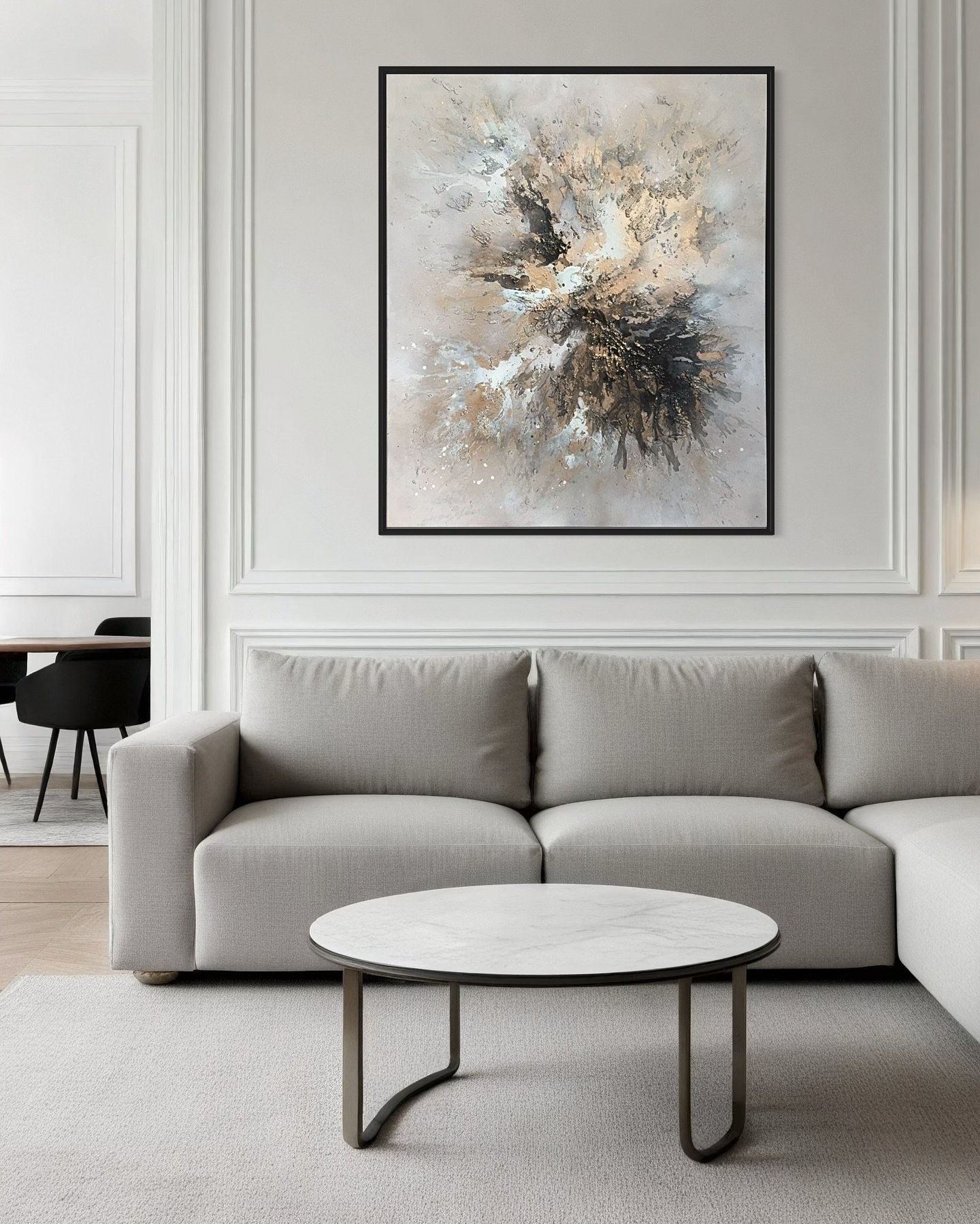 Large vertical abstract painting in black, white, and gold splatter patterns, framed in black and hung above a light grey sofa.