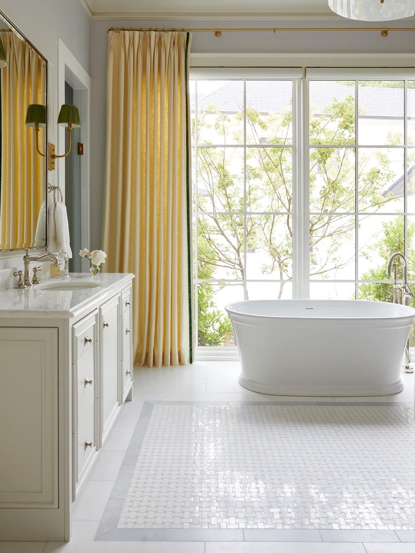 A bright, elegant bathroom with a white vanity and a floor featuring a central mosaic mat of small, woven white tile surrounded by a border of large gray and white marble tile.
