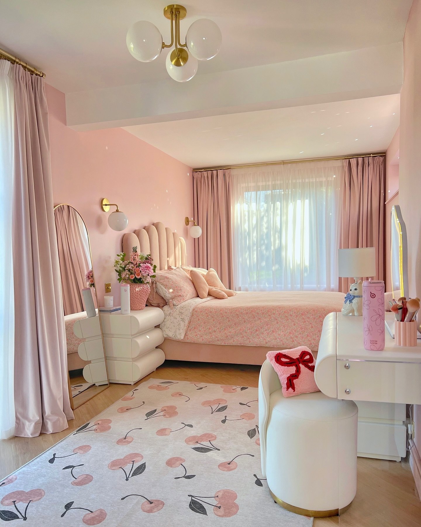 Vibrant pink bedroom with a channel-tufted velvet headboard, white stack-style nightstands, and a pink and white cherry-patterned area rug.