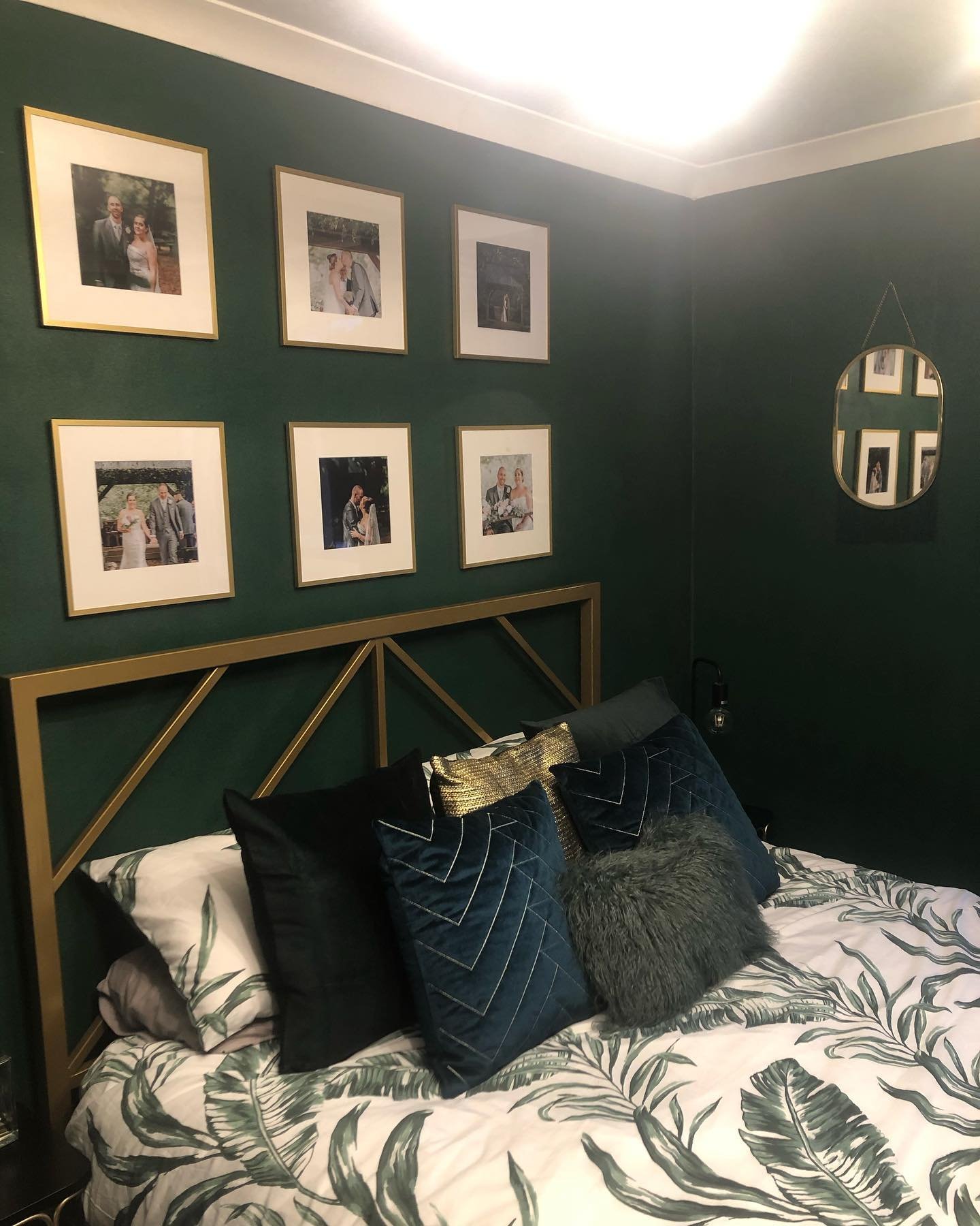 Bedroom with dark pine green walls, a gold geometric headboard, a gallery wall of framed photos, and palm print bedding.
