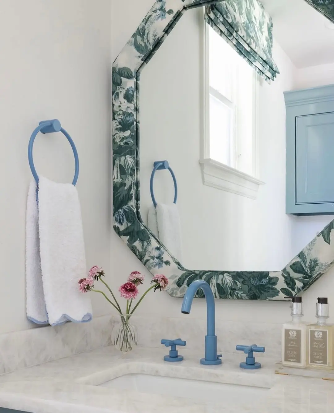 A bright powder blue colored towel ring holding a white hand towel with blue trim, mounted on a white wall above a marble counter and matching blue faucet.