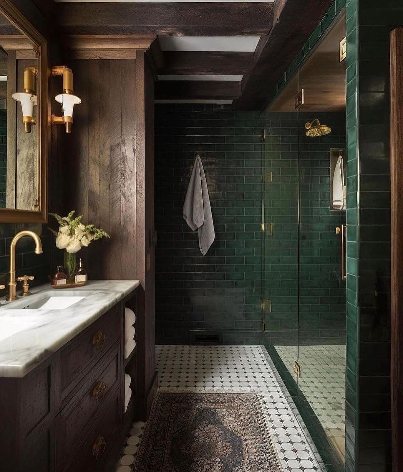 A luxurious, moody bathroom featuring dark wood paneling, a marble-top vanity, a shower with glossy emerald green subway tiles, a mosaic black and white patterned tile floor, and a small, dark rectangular patterned rug.
