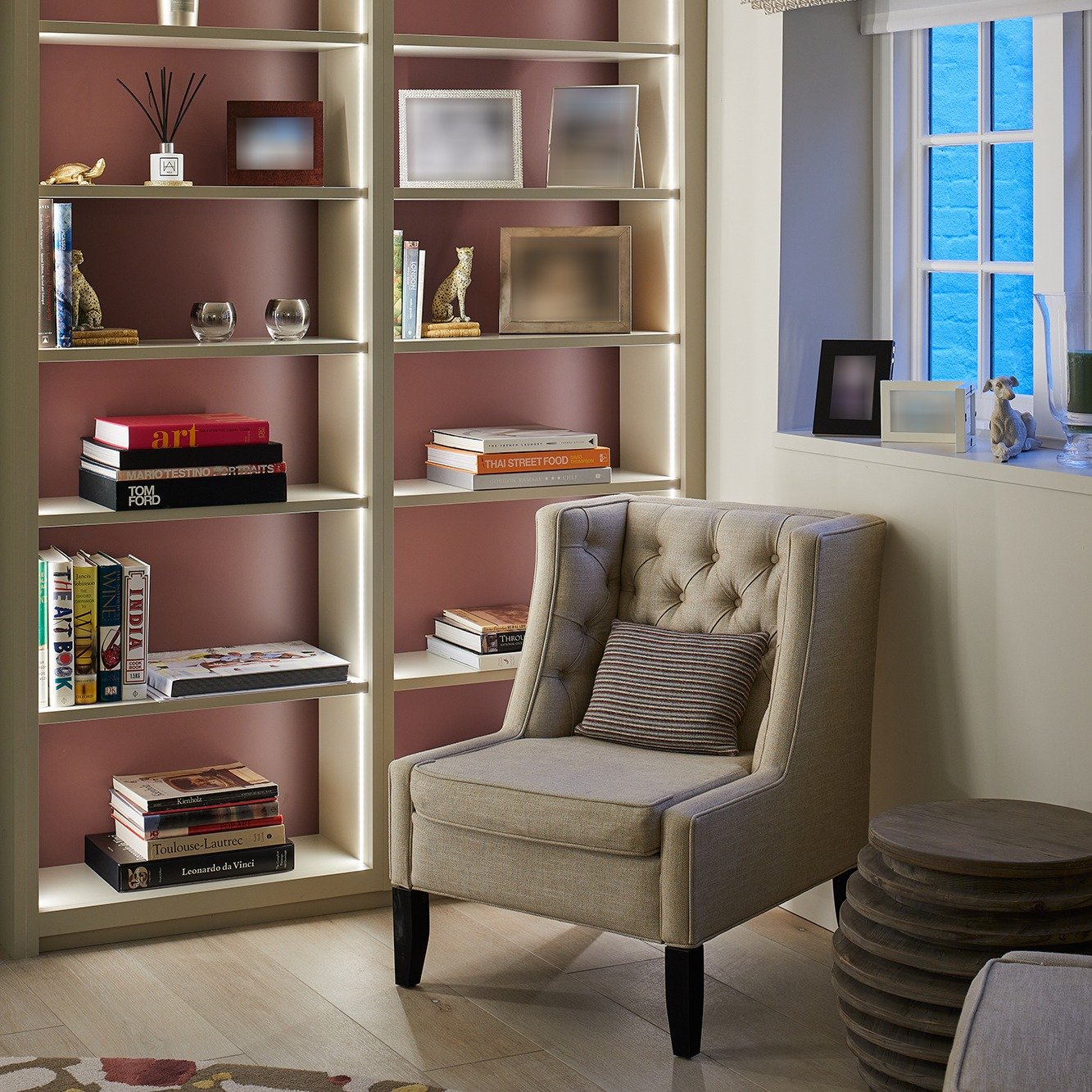 Modern reading nook with a beige tufted wingback chair, custom built-in bookshelves with strip LED lighting, and a blush pink interior backing.