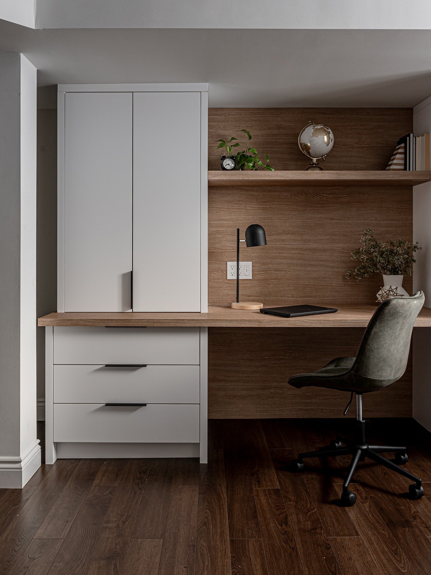 Small, modern home office nook with a light wood desk, wood plank accent wall, light gray cabinets, and a gray-green rolling office chair.
