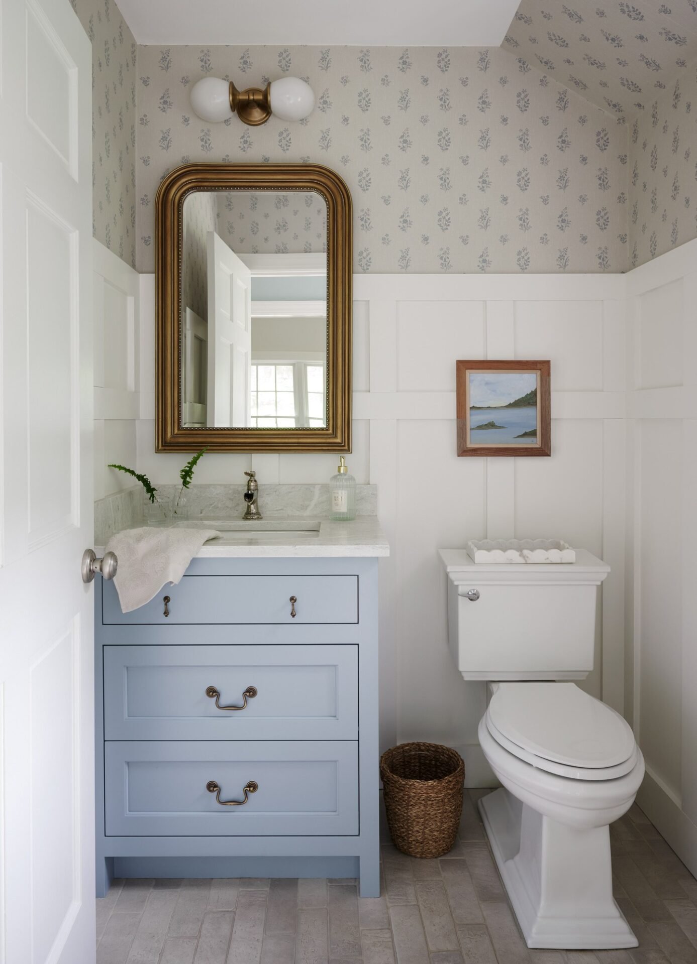 Powder room with white board-and-batten wainscoting, a light blue vanity, and small-print wallpaper above.