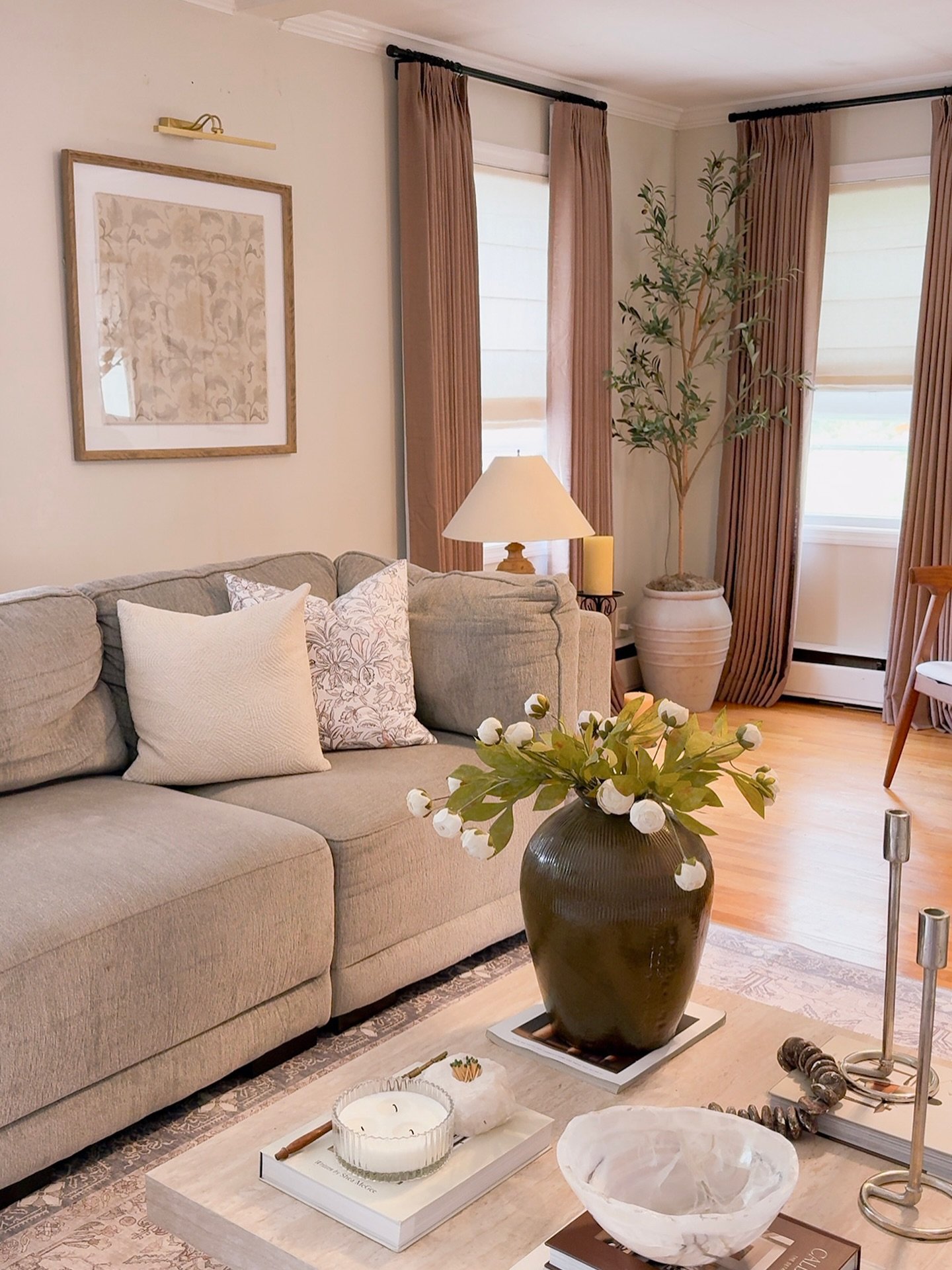 Floor-length mauve-taupe curtains hung on a black rod, layered over white window shades in a cozy neutral living room.