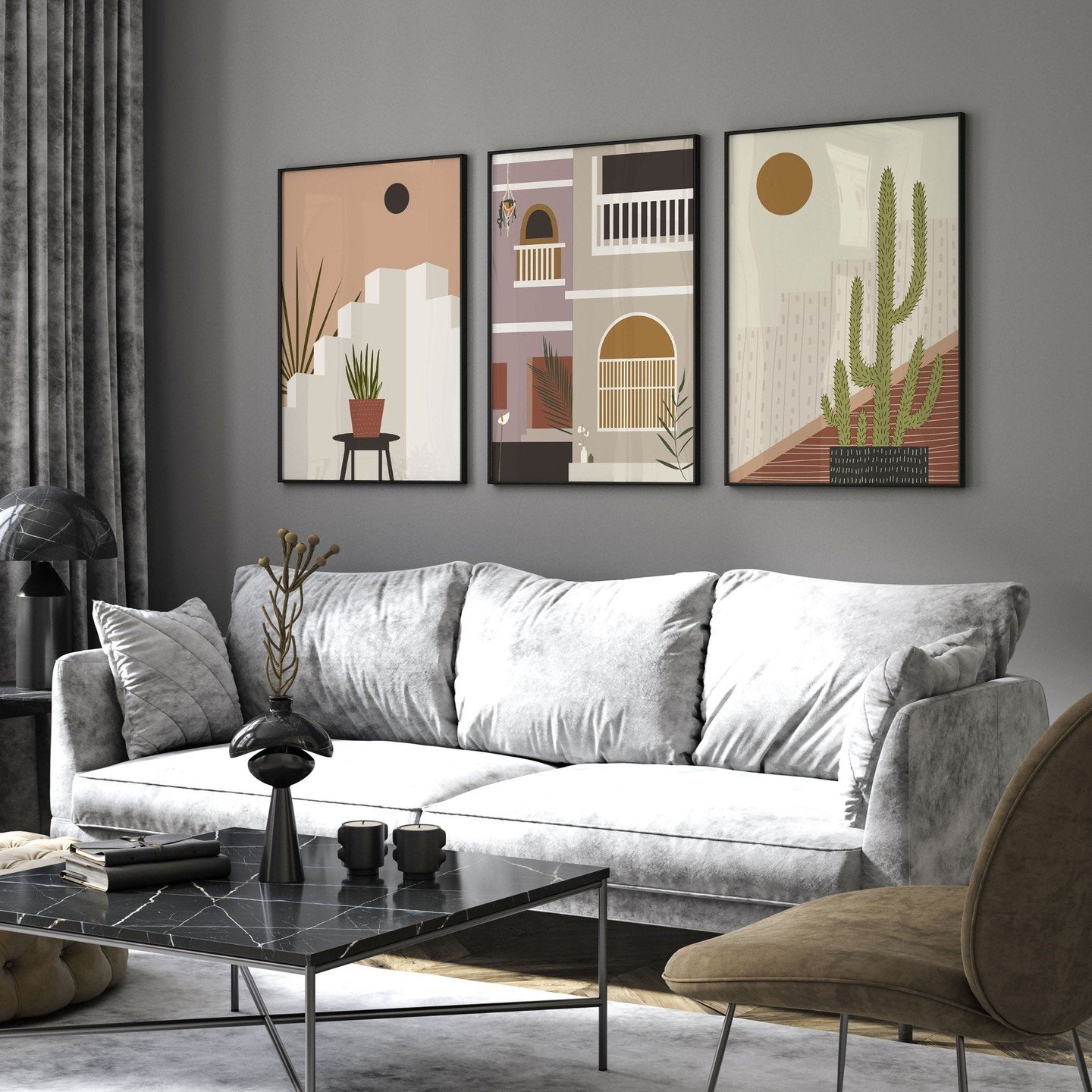 Three framed vertical art prints with desert-modern style illustrations of buildings and cactus in pink, green, and brown tones, hung over a grey sofa.