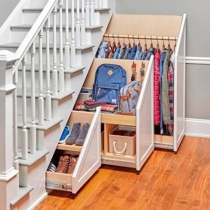 White under-stairs unit with multiple pull-out segments for coats, shoes, bags, and accessories.