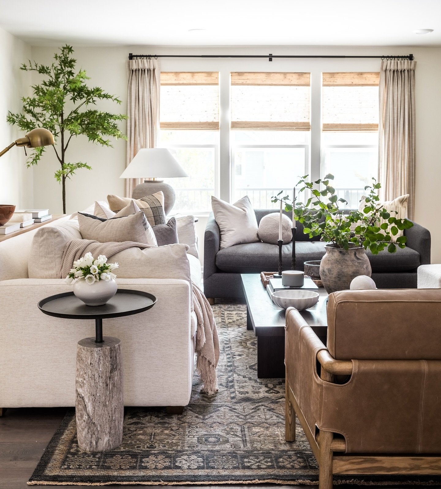 A cozy living room featuring facing white and charcoal gray sofas, a dark patterned rug, leather accent chair, and natural woven wood blinds.