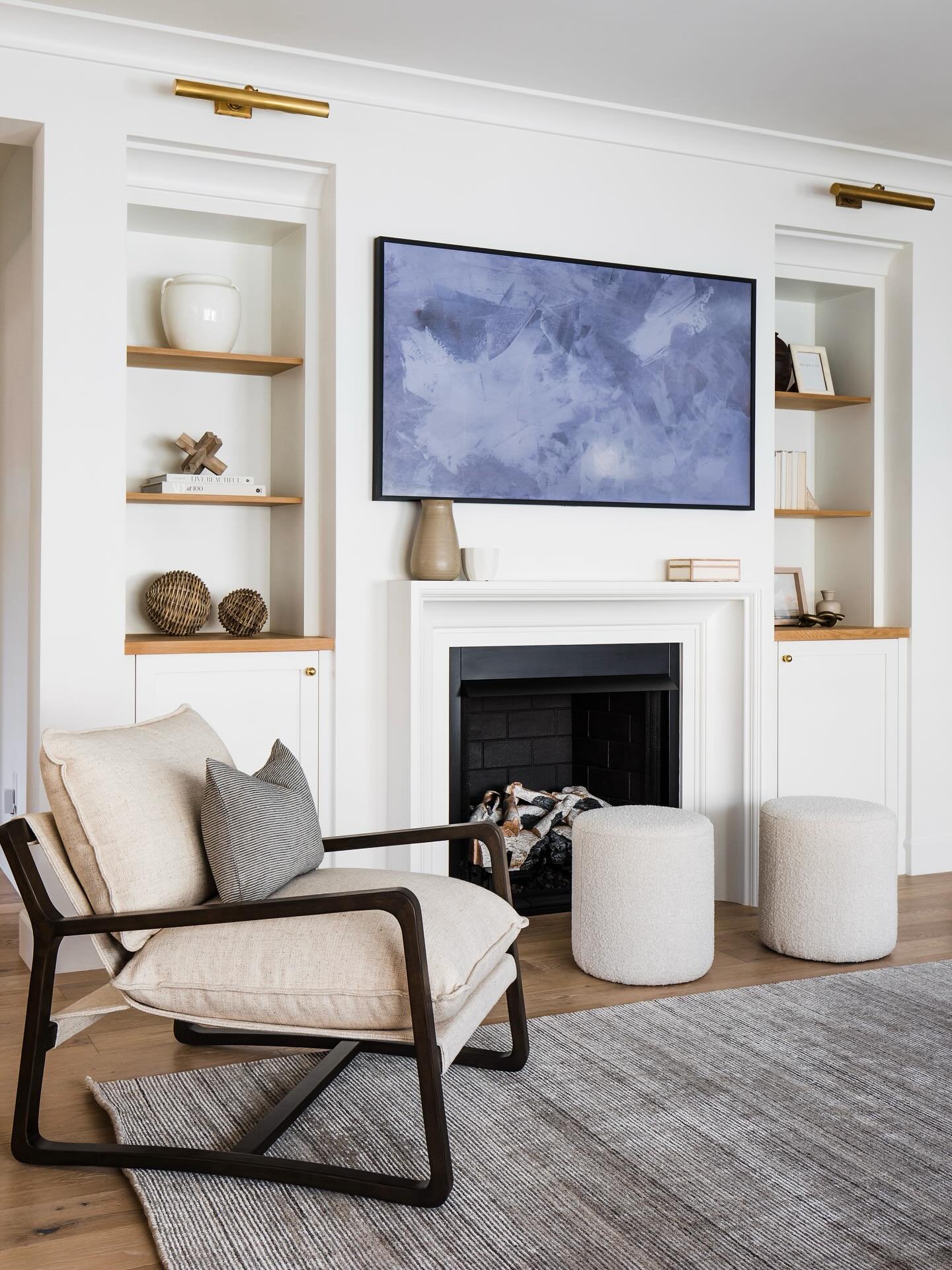 Living room with a white traditional fireplace, black firebox, white built-in cabinets with light wood open shelving, and a modern lounge chair.