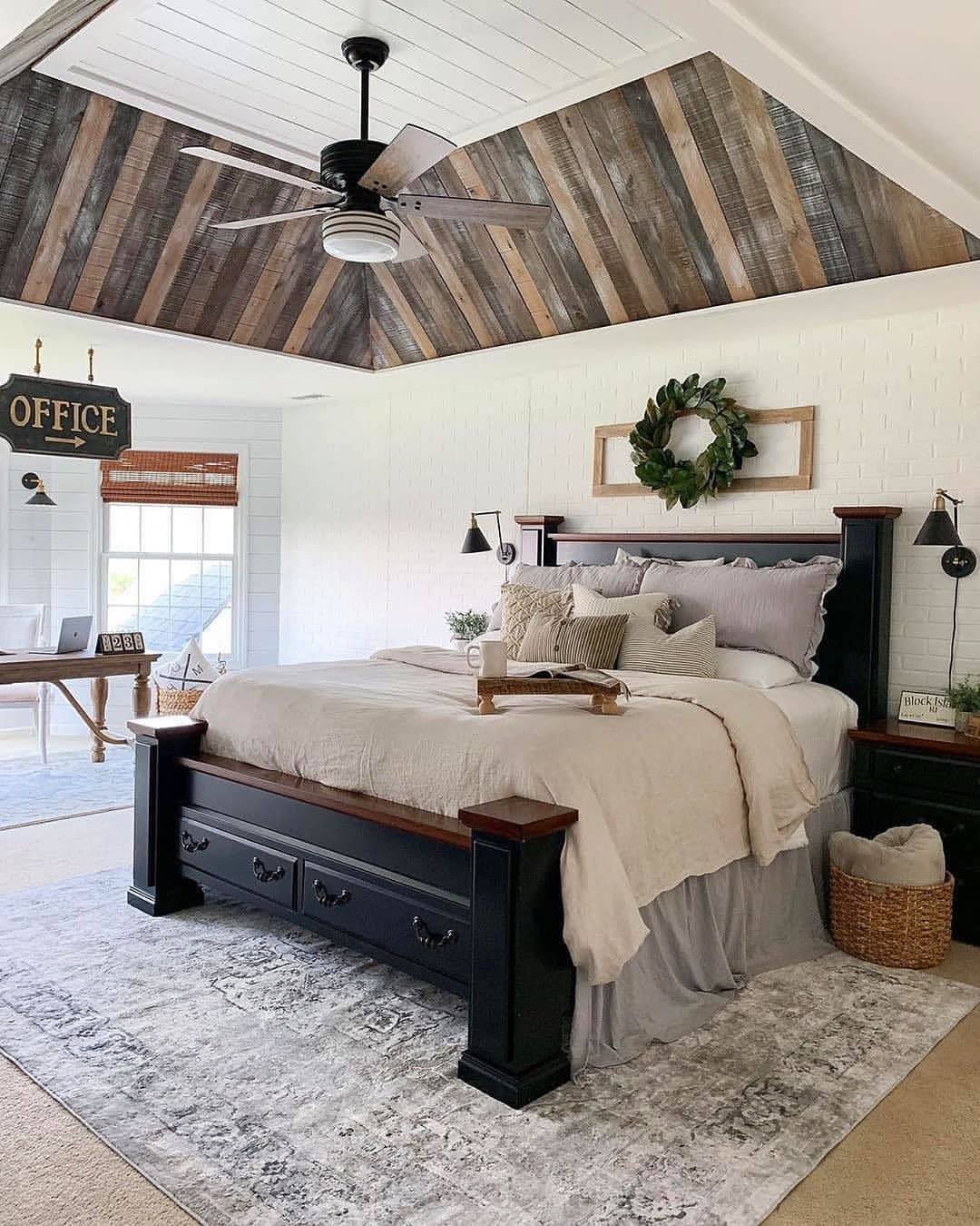 Bold farmhouse bedroom with a vaulted ceiling clad in mixed reclaimed wood. Features a black four-poster bed and a brick accent wall.