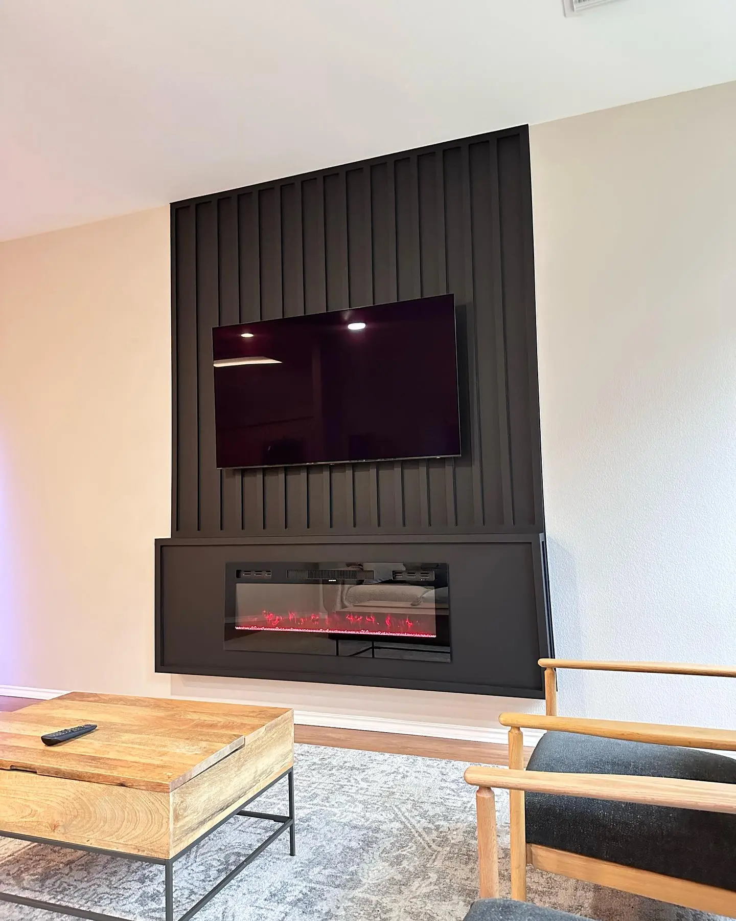 Contemporary living room with a feature wall made of black vertical wood slat paneling, a protruding black surround containing an electric fireplace, and a mounted flatscreen TV.
