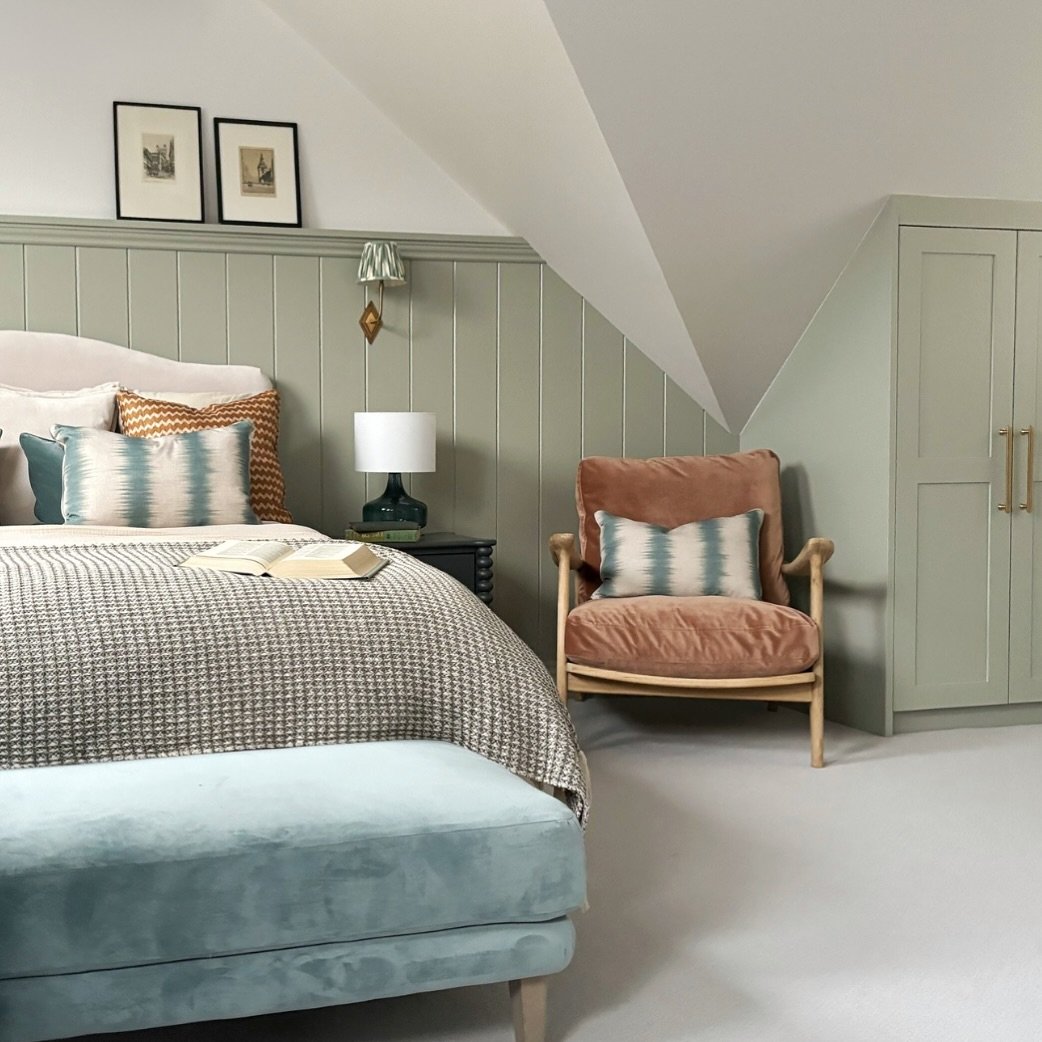 Attic bedroom with a sloped ceiling, vertical sage green paneled wall, matching sage built-in wardrobes, and blue velvet bench.