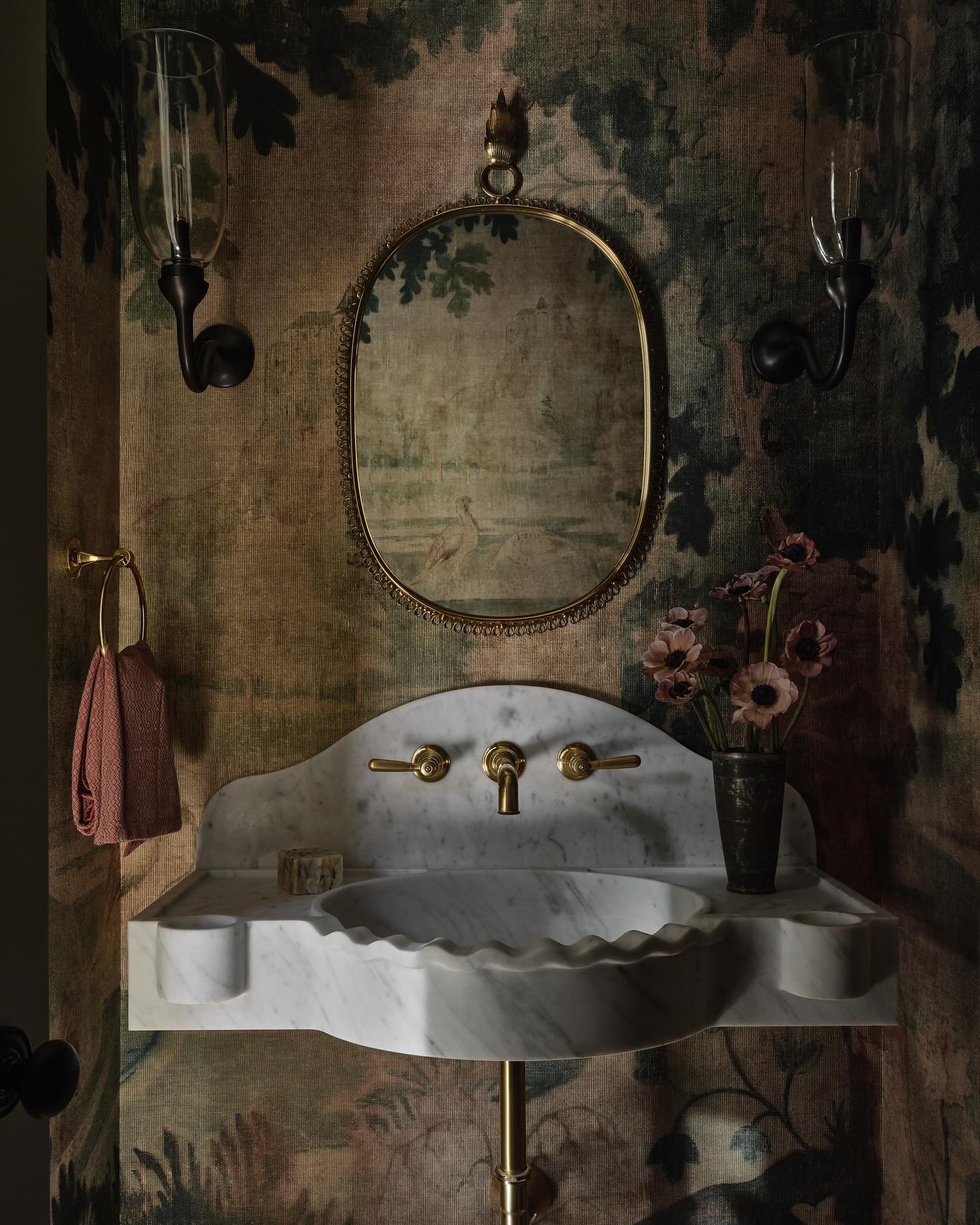 Floating white marble sink with a scalloped basin edge, set against dark, dramatic tapestry-style forest wallpaper.