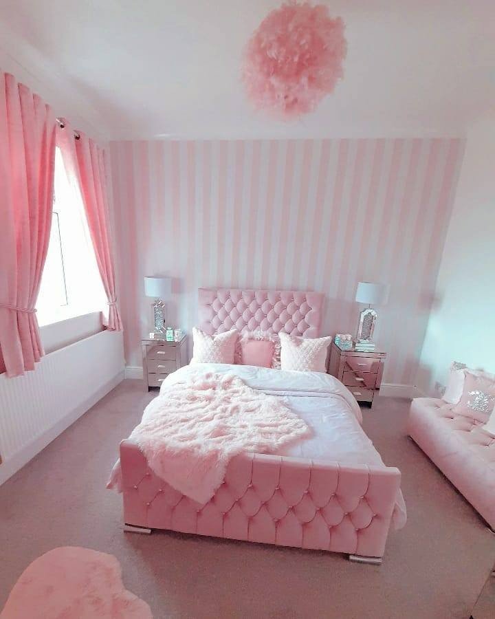 Bedroom featuring a pale pink and white striped accent wall, a fully tufted pink velvet bed, and mirrored nightstands.