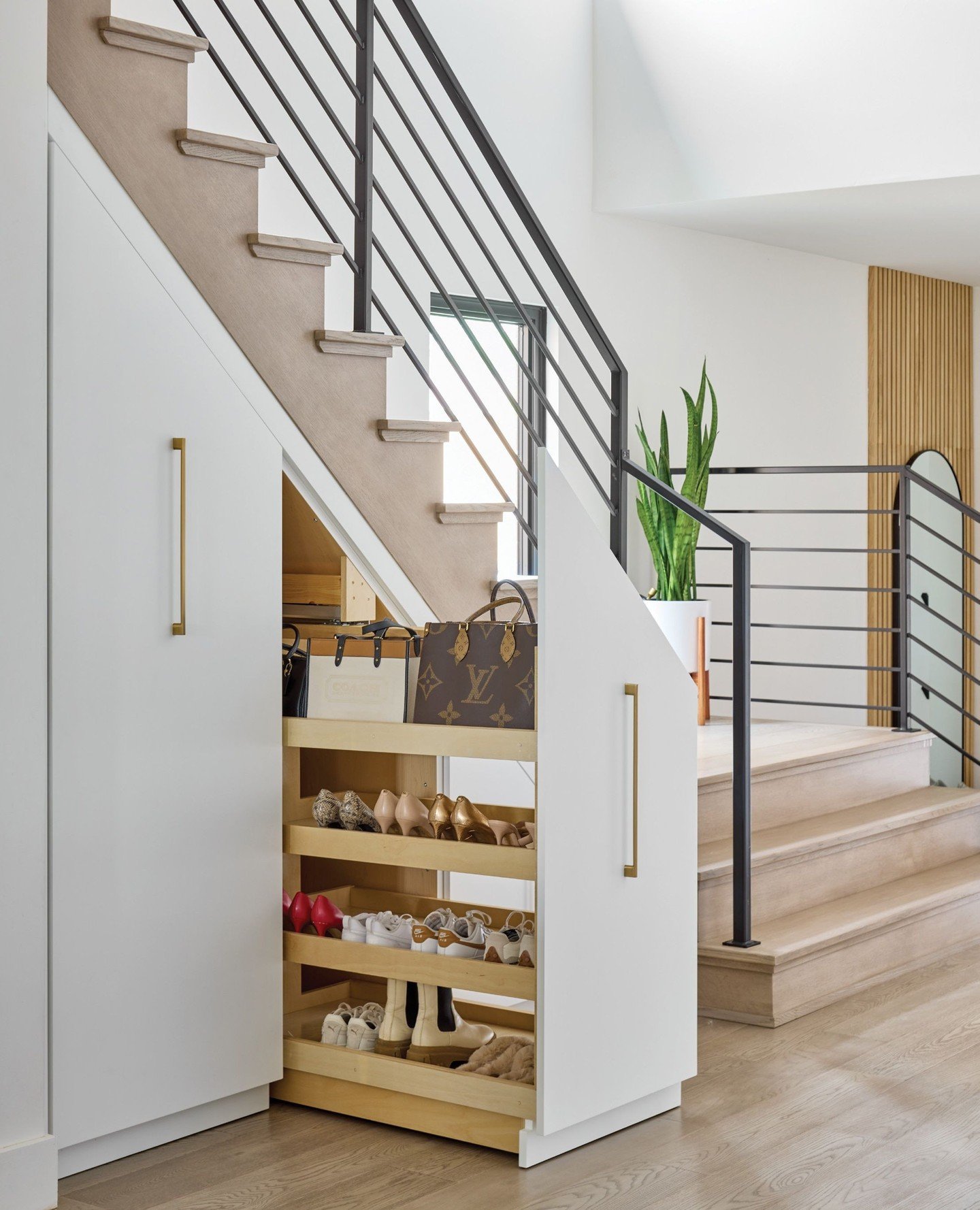 Custom white cabinet built under a staircase with a large wooden drawer pulled out, showing four tiered shelves of shoes.