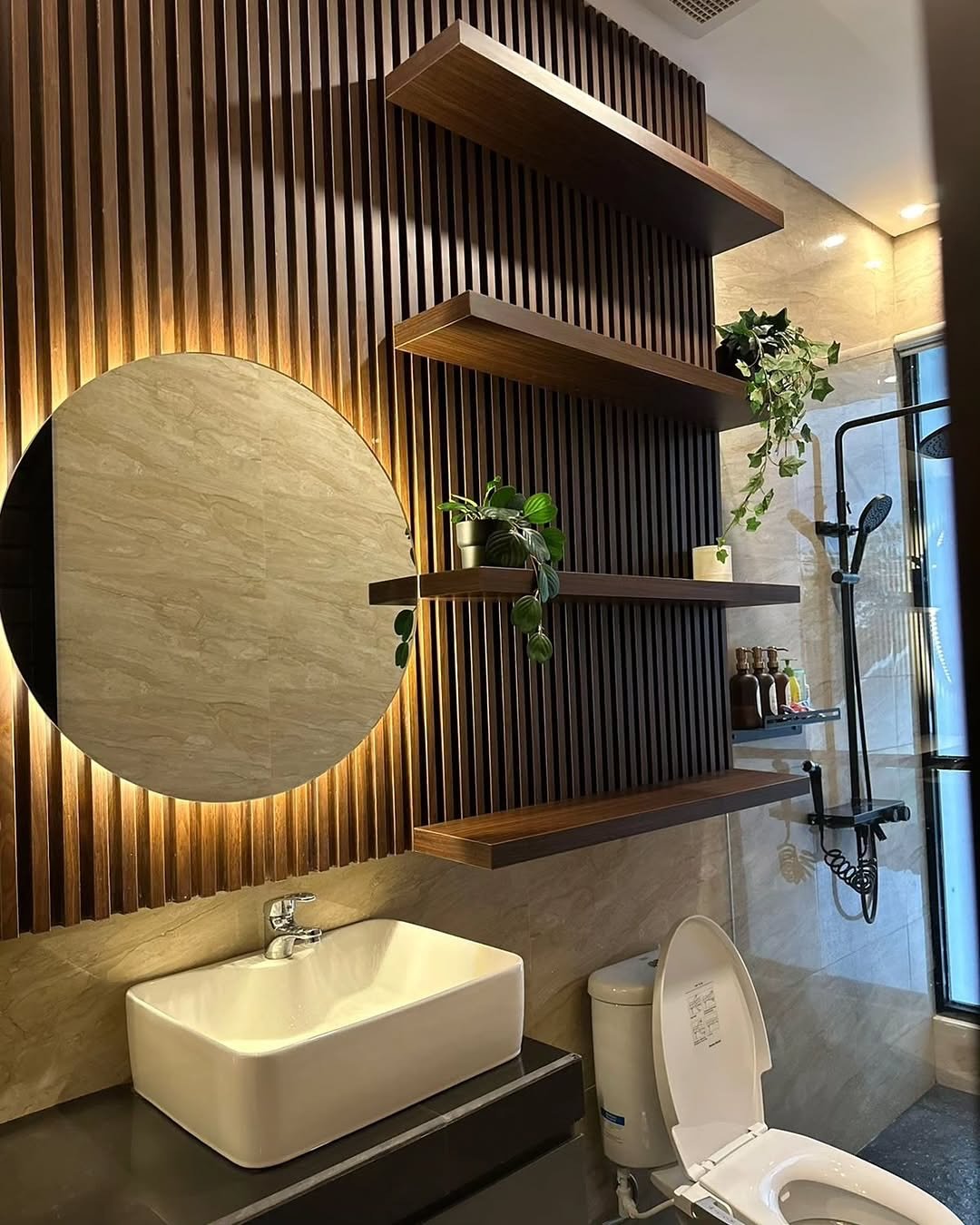 Four dark wood floating shelves installed against a dramatic dark brown vertical wood-slat accent wall, with a backlit round mirror to the left.