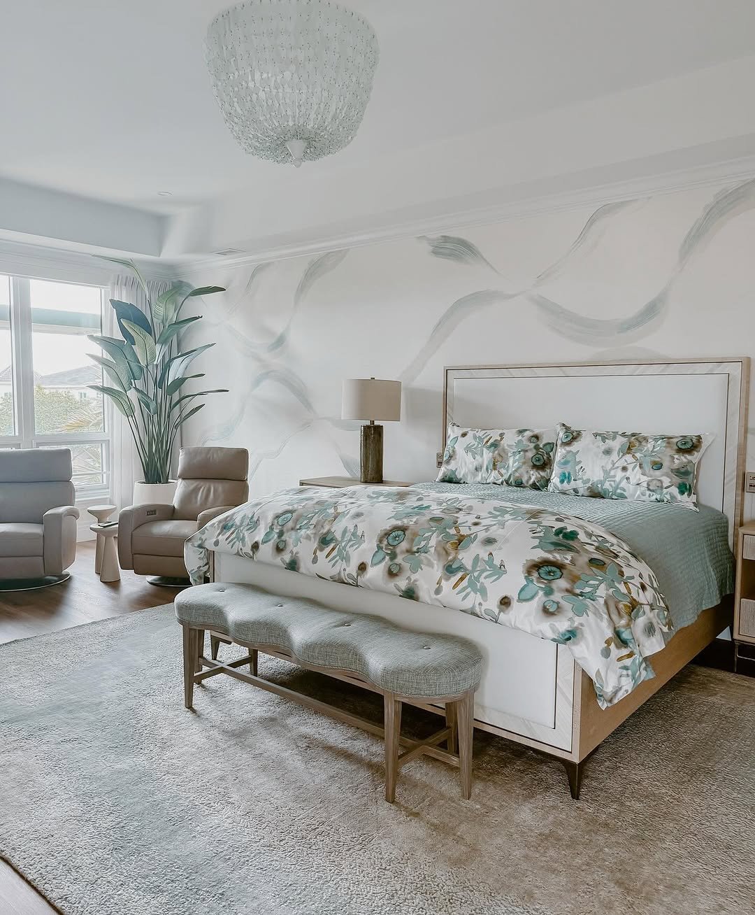 A bright, modern bedroom with a watercolor-style mural and a low bench with a gray fabric cushion and light wood frame at the end of the bed.