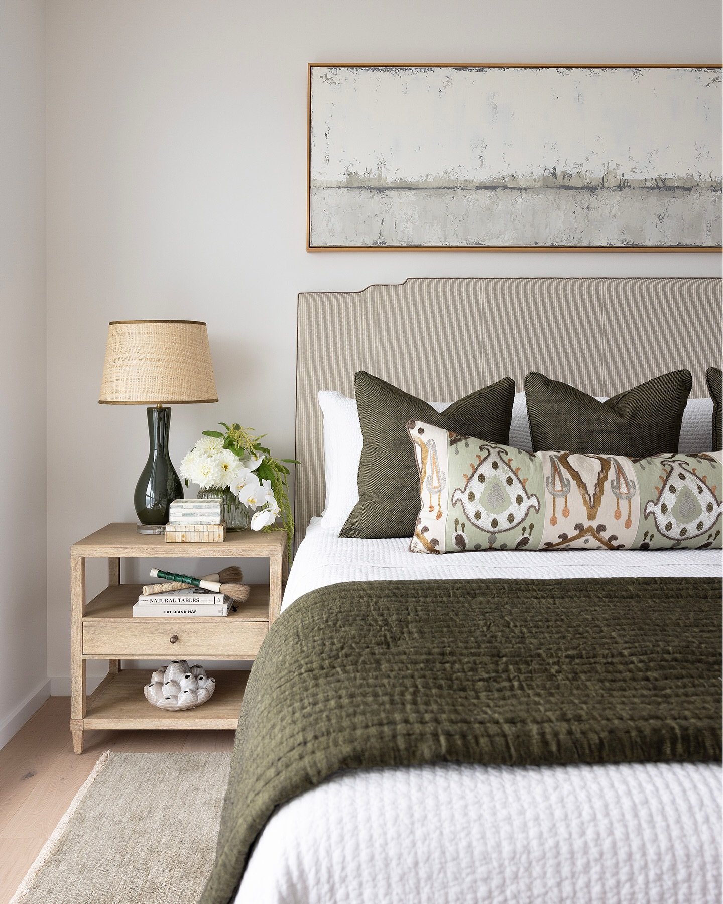 Modern bedroom with white walls, a striped upholstered headboard, and olive green bedding and accent pillows.