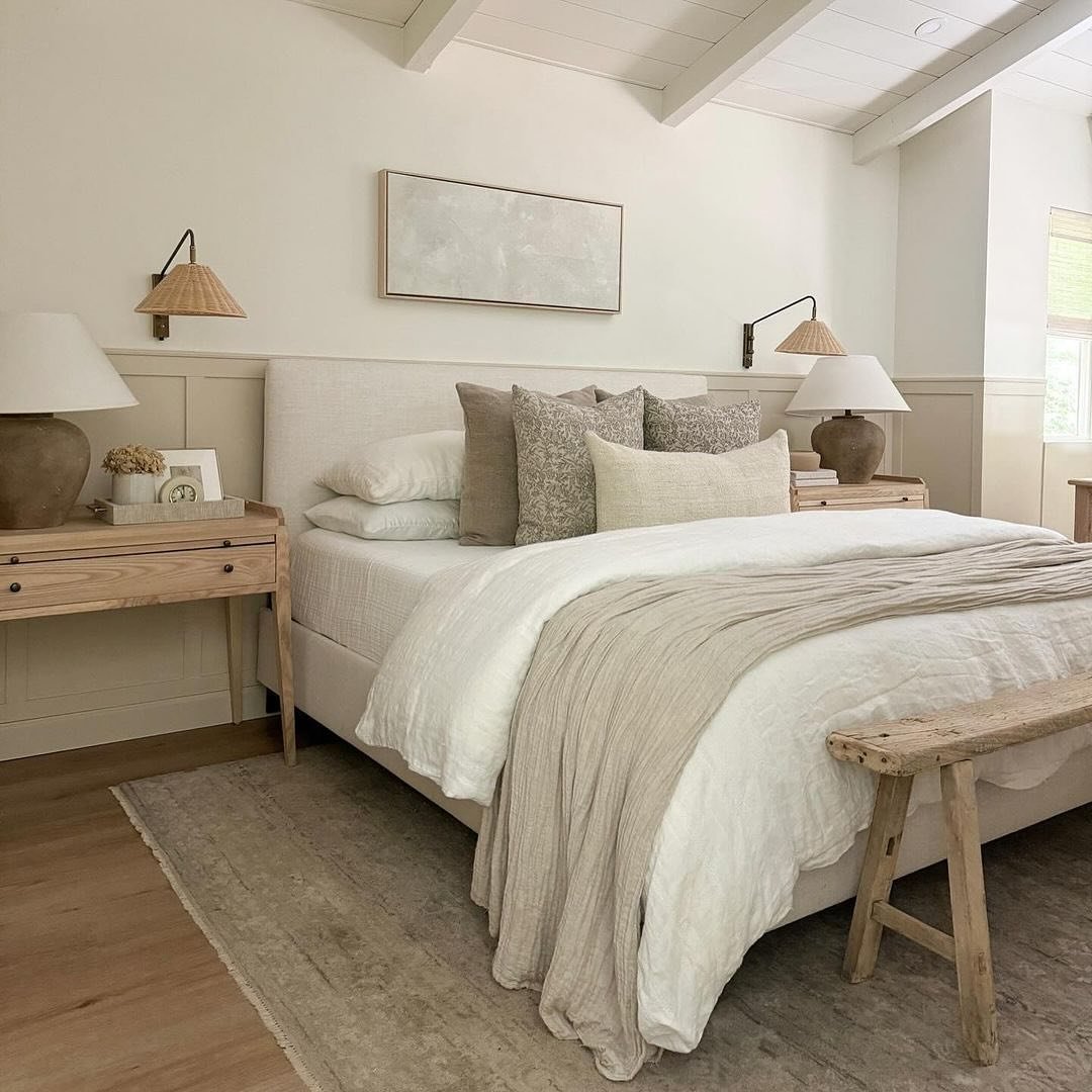 Bedroom with a vaulted ceiling, tongue-and-groove paneling, pale wood nightstands, a raw wood bench, and textured white and beige bedding.