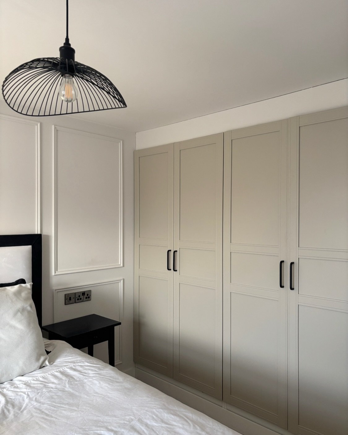 Built-in bedroom wardrobe in a light greige color with simple panel doors and long matte black bar handles.