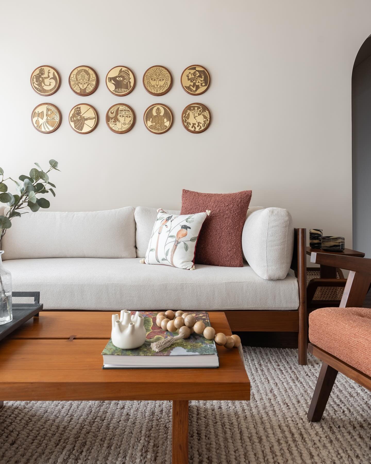 Symmetrical arrangement of ten small, round gold and wood medallions depicting stylized portraits, hung above a white wooden sofa.