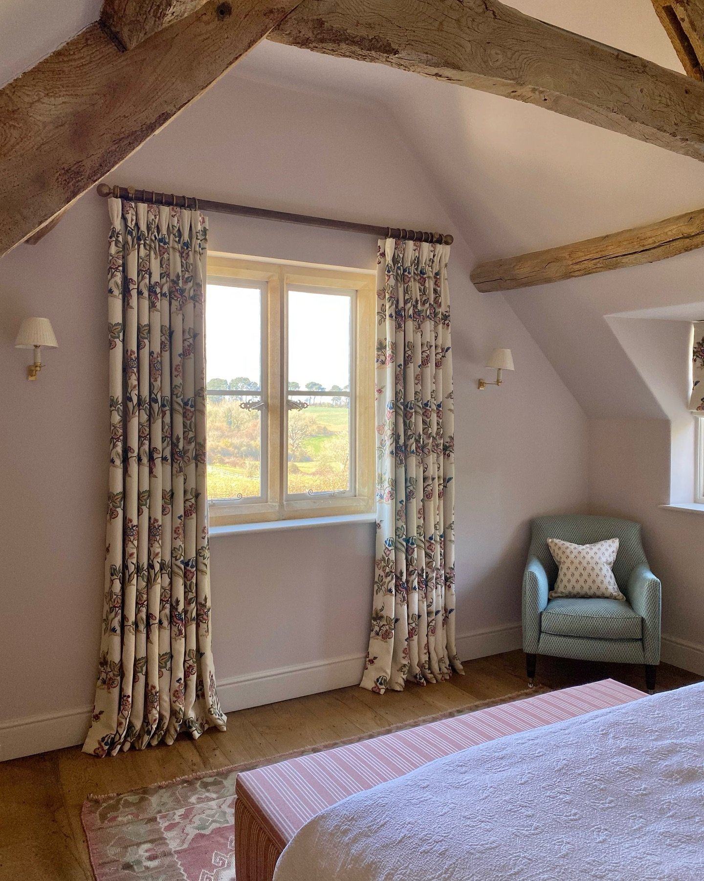 Floral pinch-pleat curtains framing a window in an attic bedroom with wood beams.