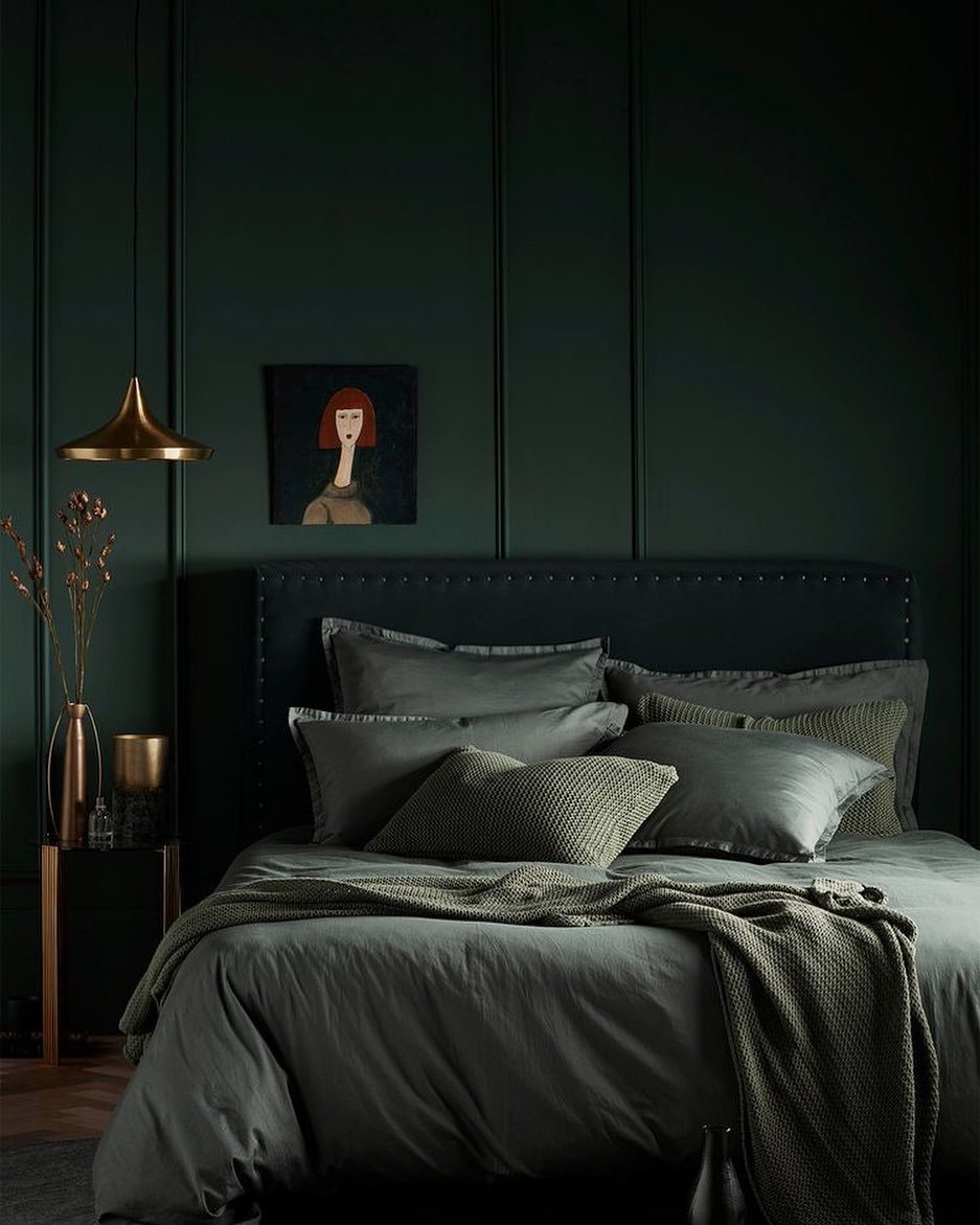 Dark bedroom with deeply painted emerald green walls, vertical wall paneling, deep green and grey bedding, a black nail-head trim headboard, and brass accents.