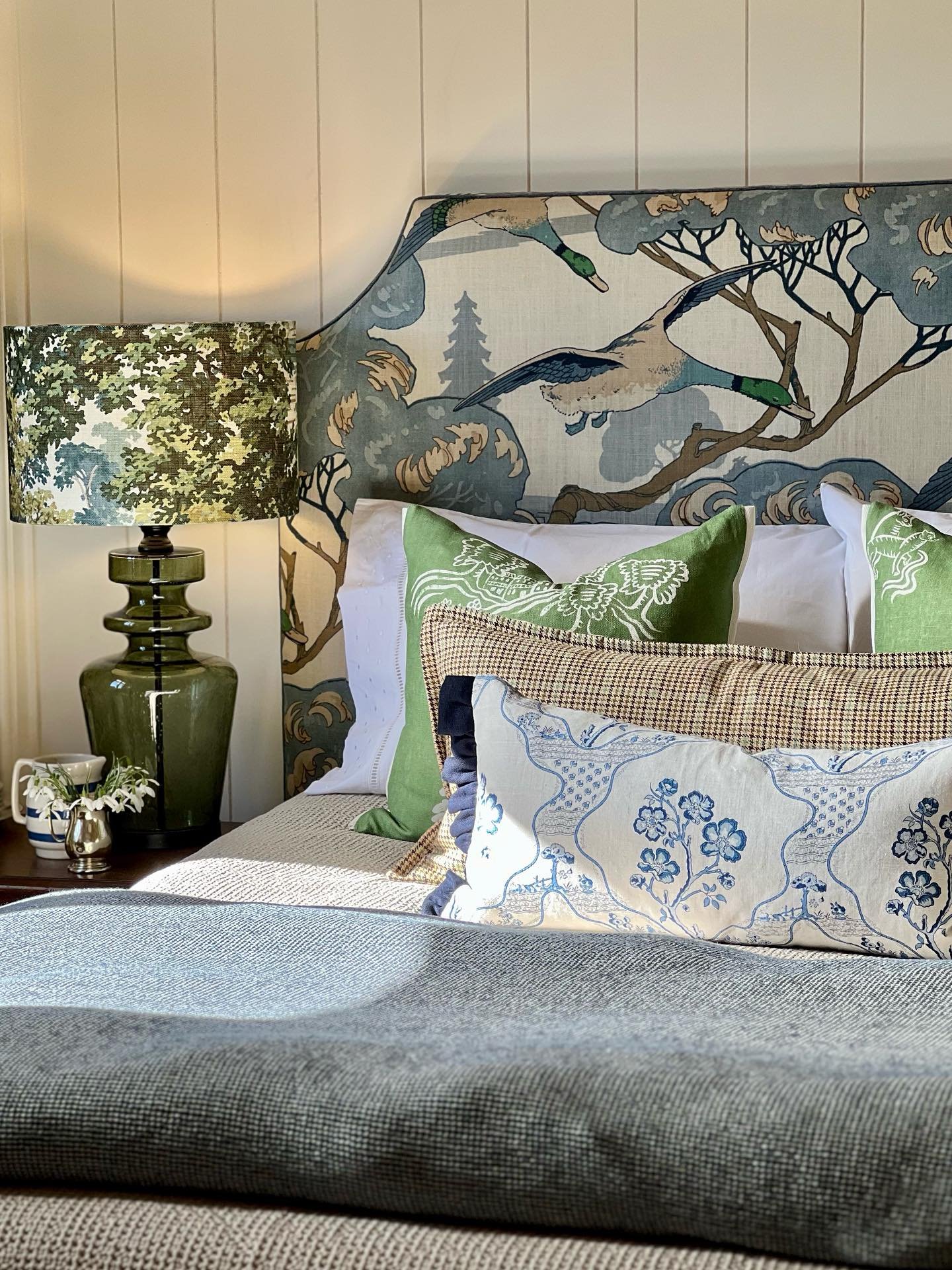 Arched headboard upholstered in a large-scale scenic fabric featuring flying ducks and trees in shades of blue, green, and brown, set against white vertical shiplap.