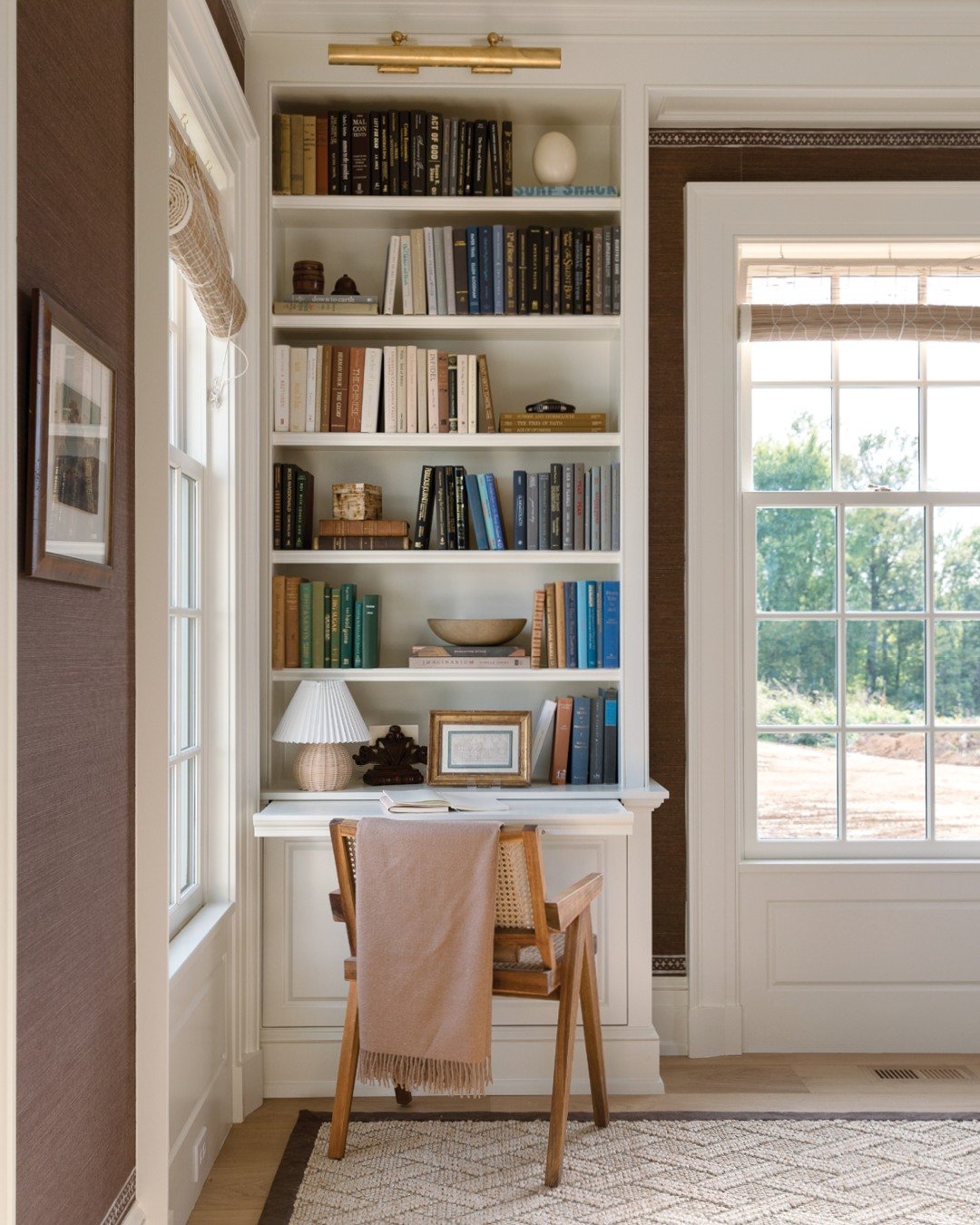 Traditional reading and writing nook with a white built-in bookcase, a recessed secretary desk area, and a light wood and cane chair.